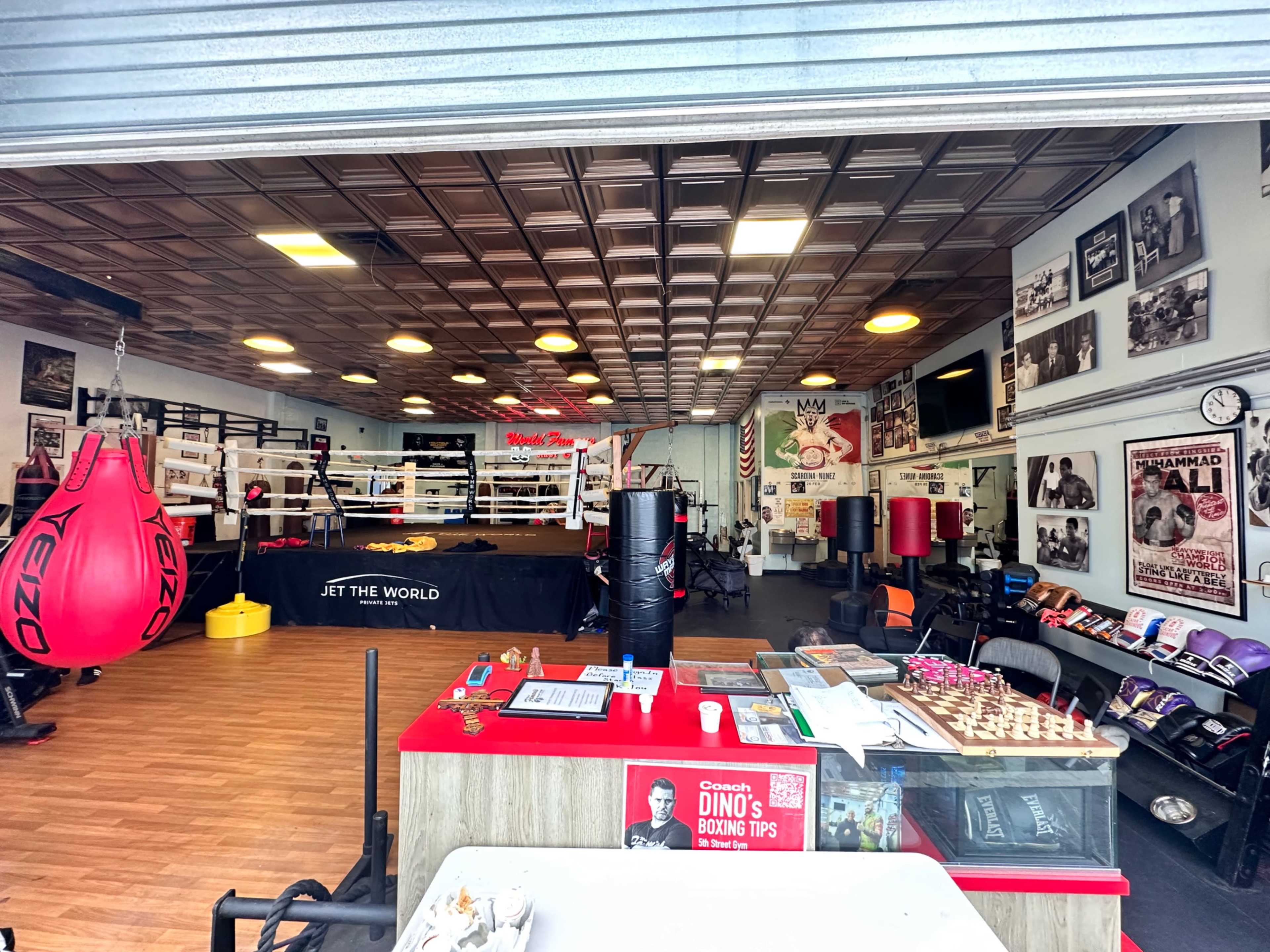 A boxing gym with a boxing ring in the background, training equipment, and various boxing-themed decorations on the walls.