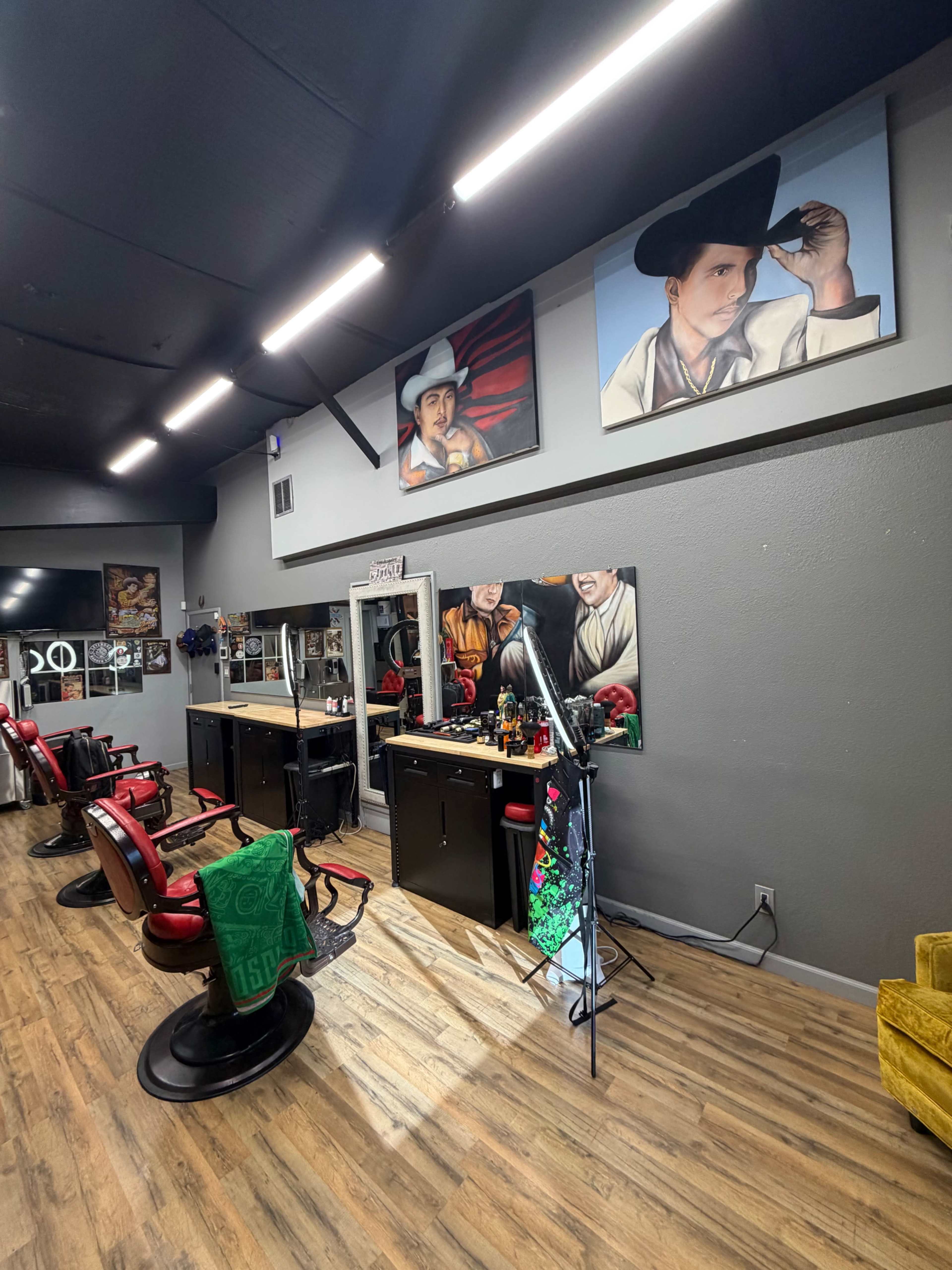 The image shows a modern barber shop with red barber chairs, a mirrored station, and artistic paintings on the walls.