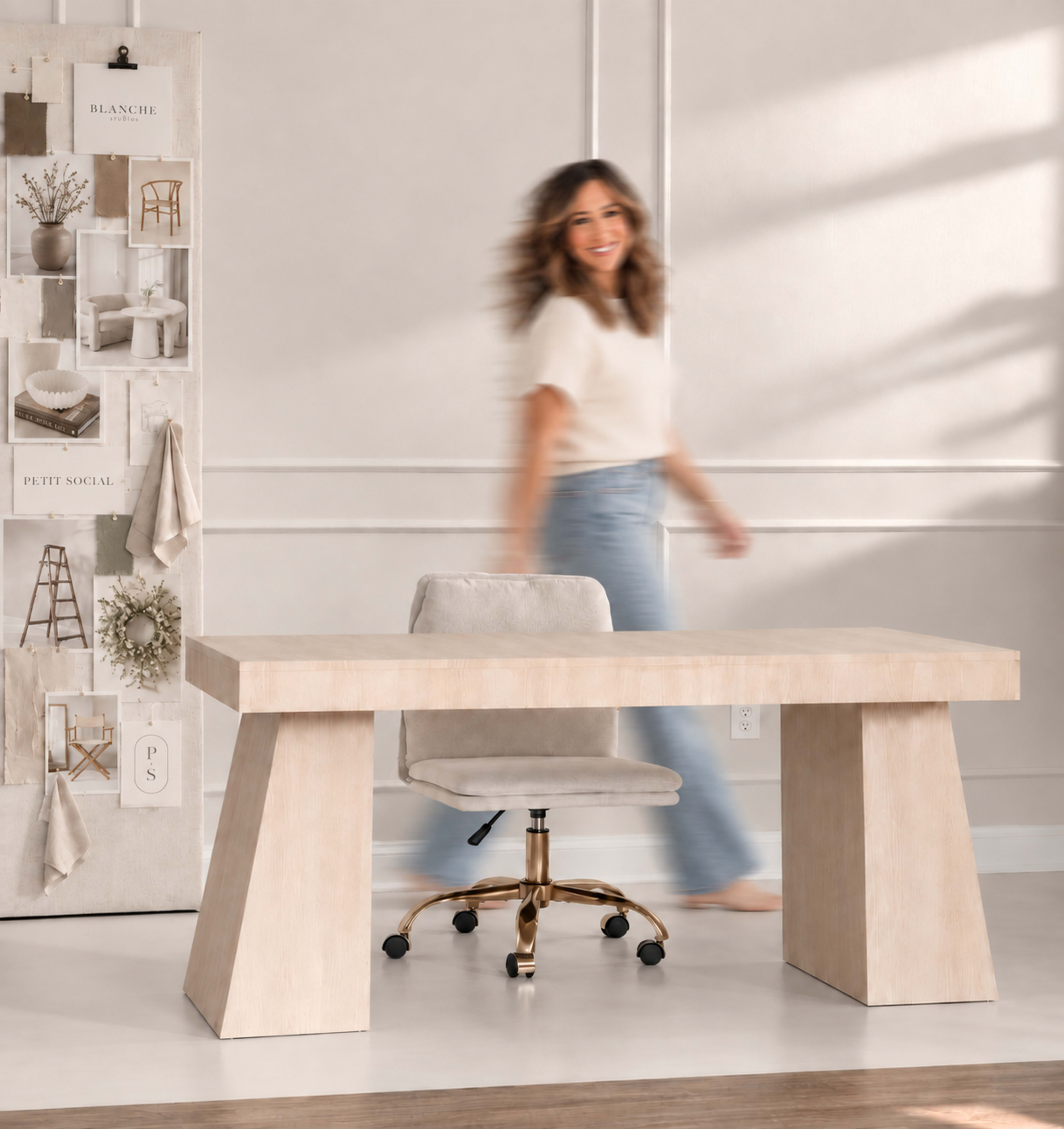 A person walks past a light-colored desk with a wheeled chair in a softly lit room displaying a wall of decor samples.