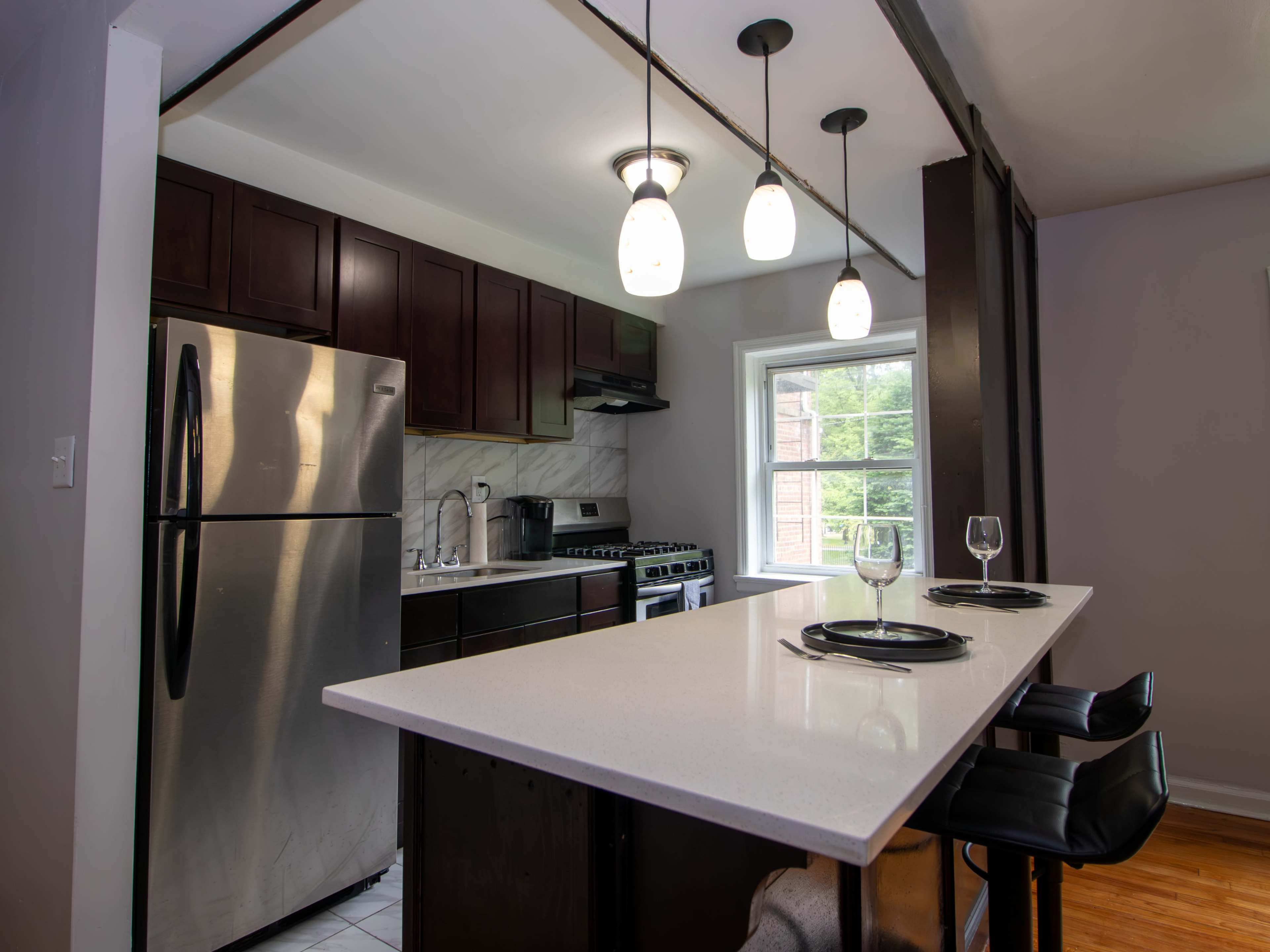 A modern kitchen features dark wood cabinets, stainless steel appliances, and a white countertop with bar seating.