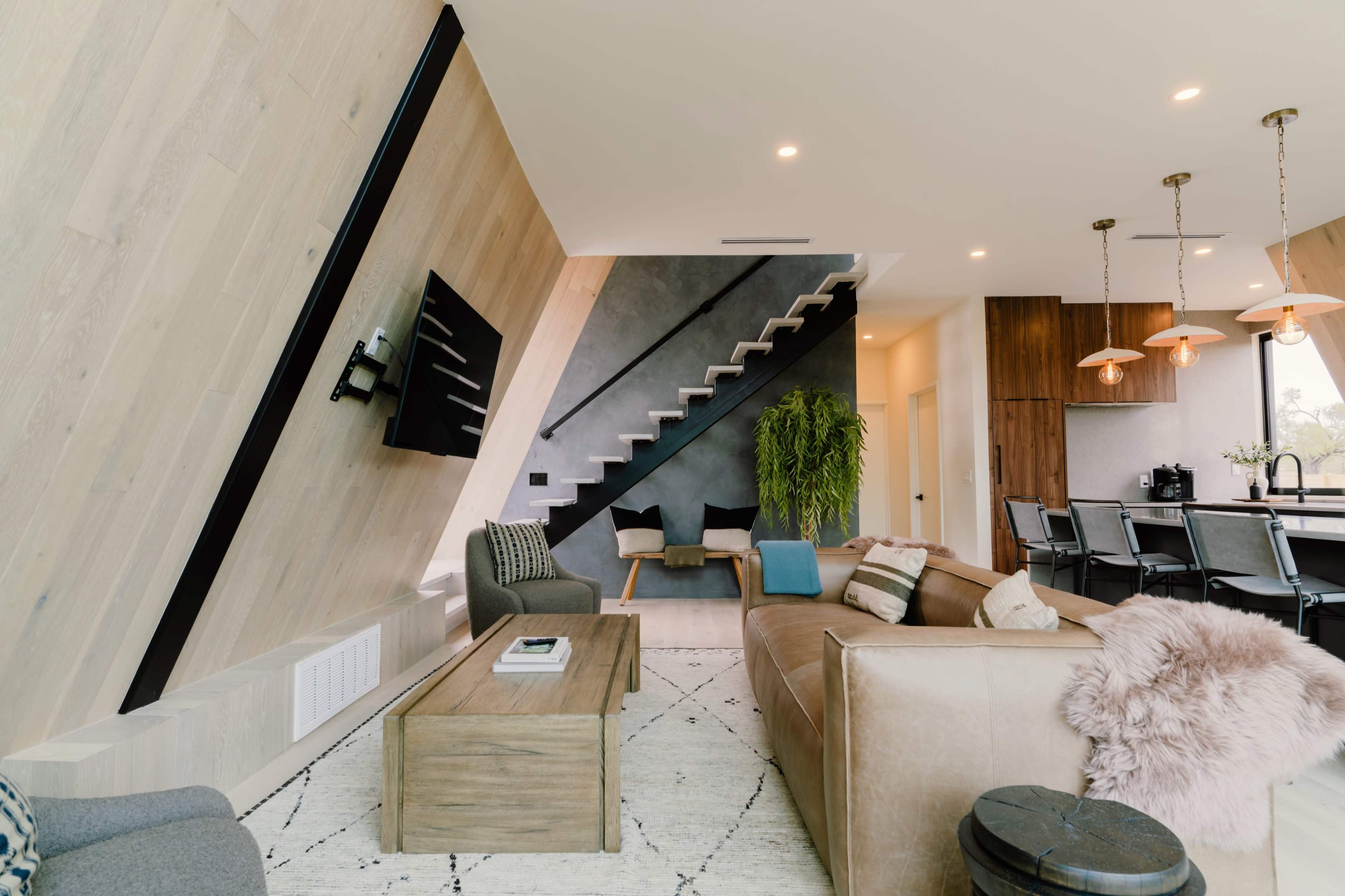 A modern living space featuring a brown leather sofa, a wooden coffee table, and a staircase leading to an upper level.