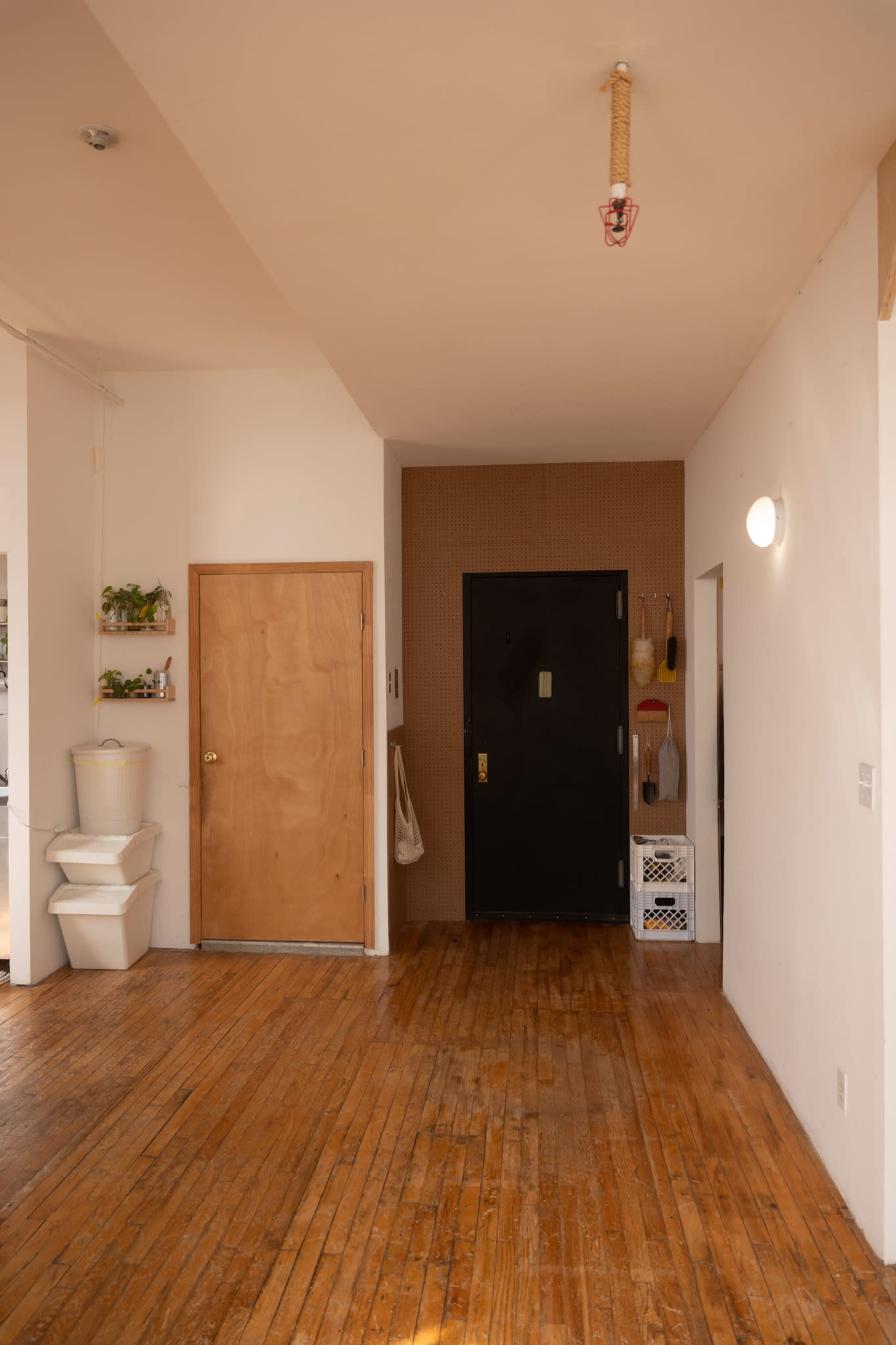 A wooden-floored entryway with a door on the left, a black entrance door straight ahead, and a toilet in the corner.