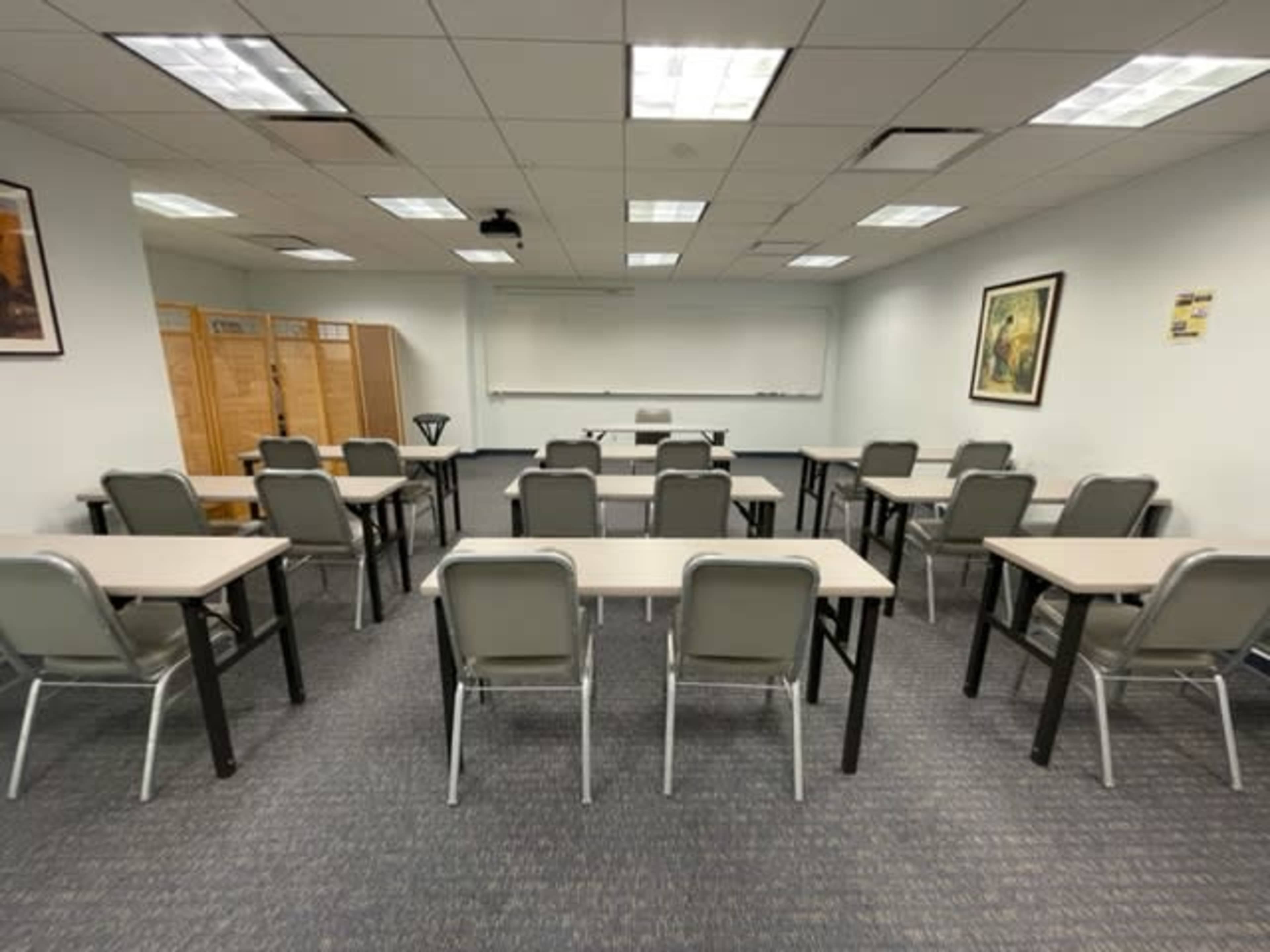 A classroom with several rows of tables and chairs facing a whiteboard at the front.