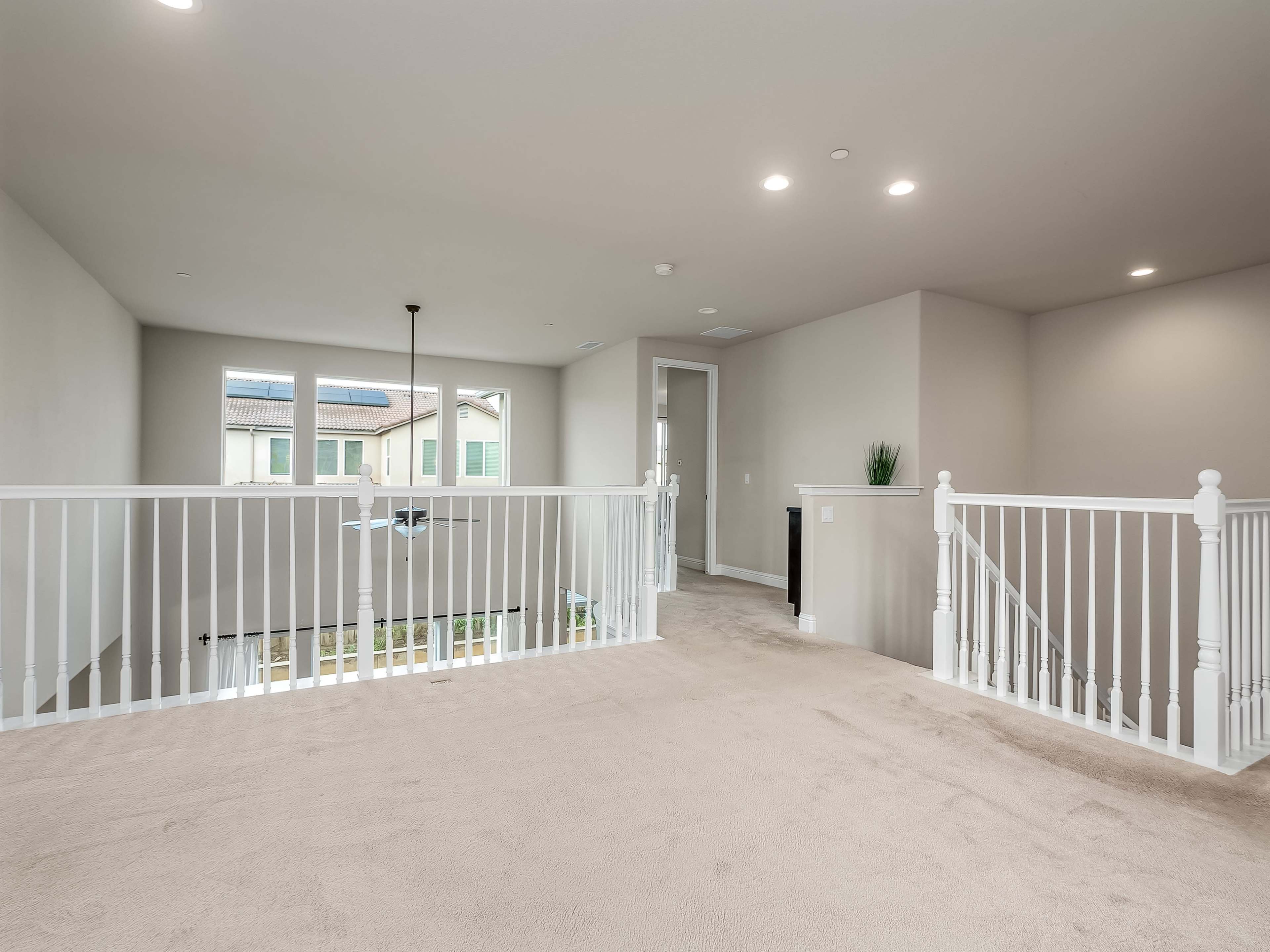 A spacious, well-lit upstairs landing with white railings and beige carpeting.