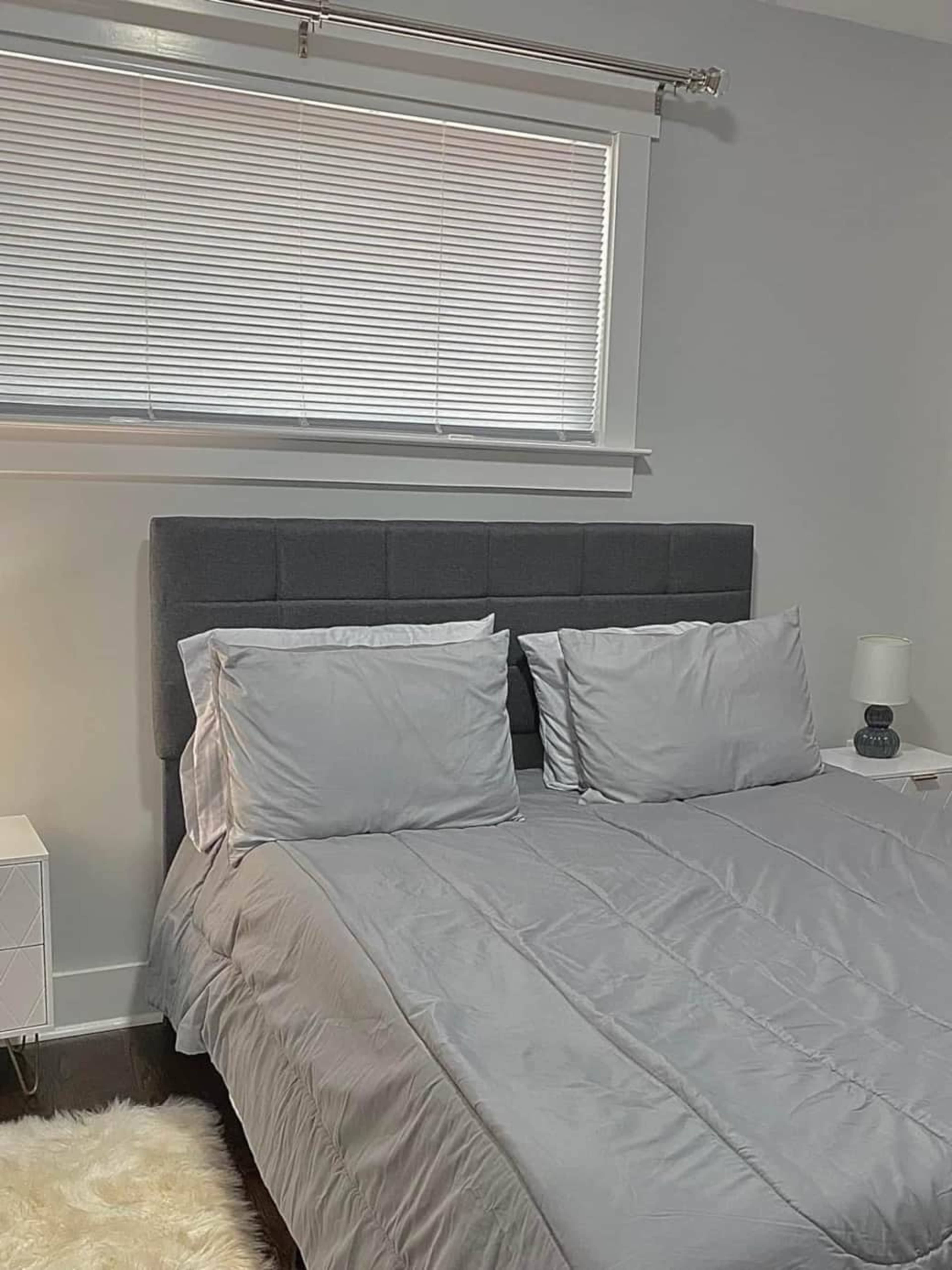 A neatly made bed with gray bedding and two pillows is positioned against a wall in a well-lit bedroom.