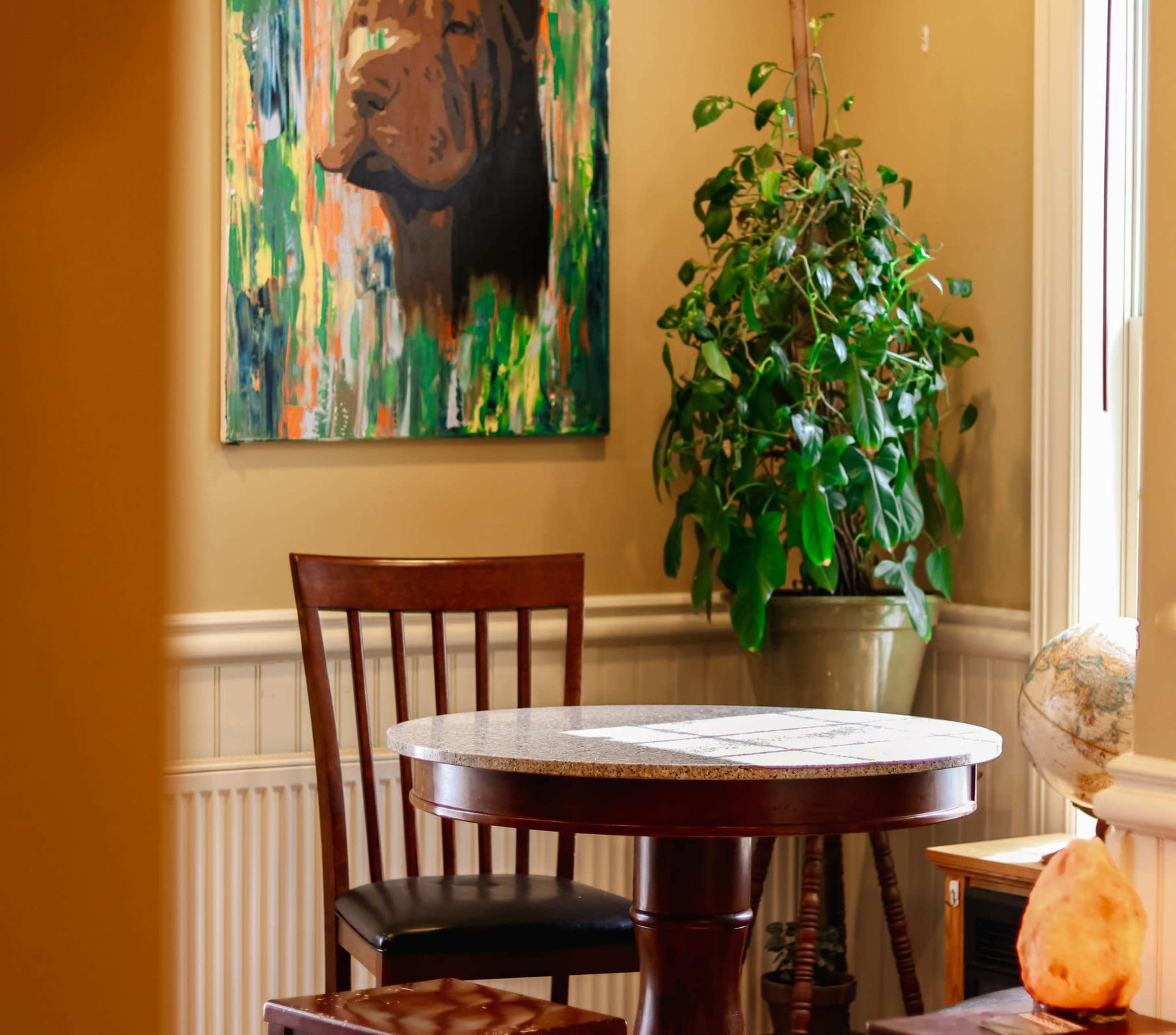 A small, round table with a granite top is positioned beside a potted plant in a room featuring a colorful dog portrait on the wall.
