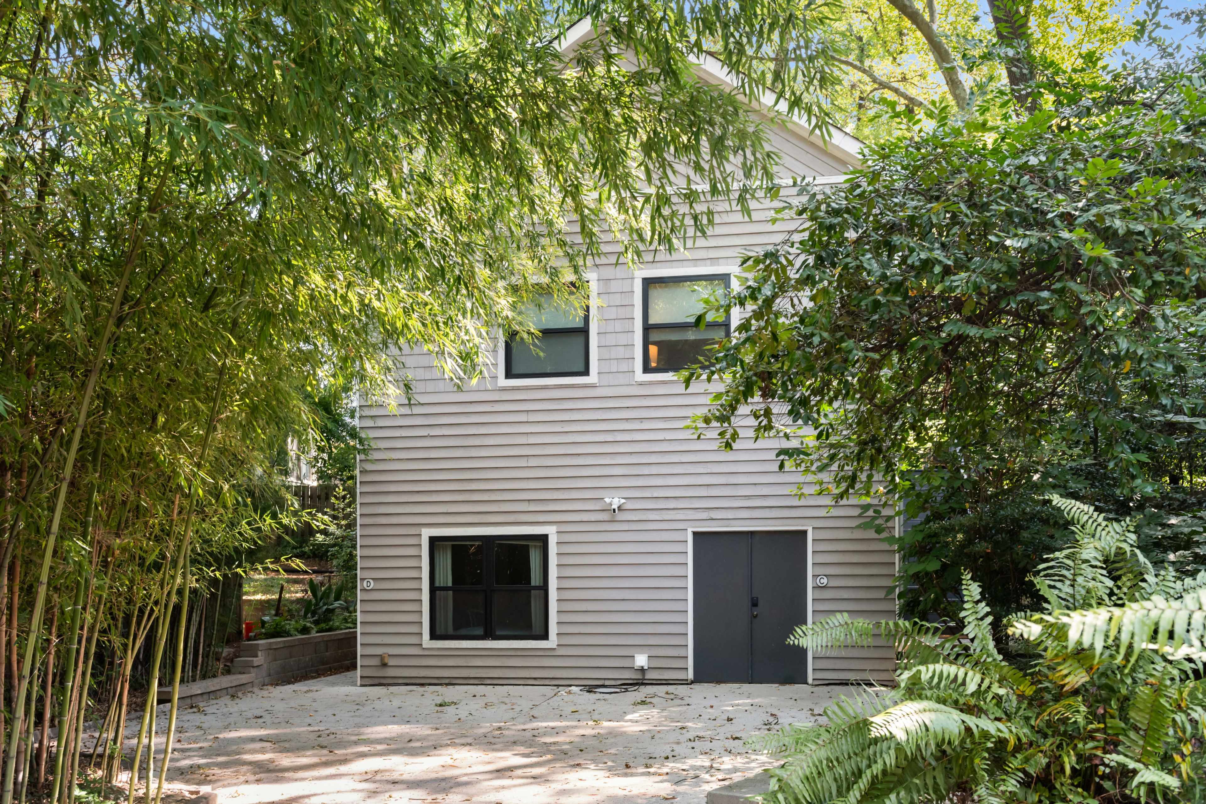 A two-story house with light gray siding is partially obscured by bamboo and other vegetation.