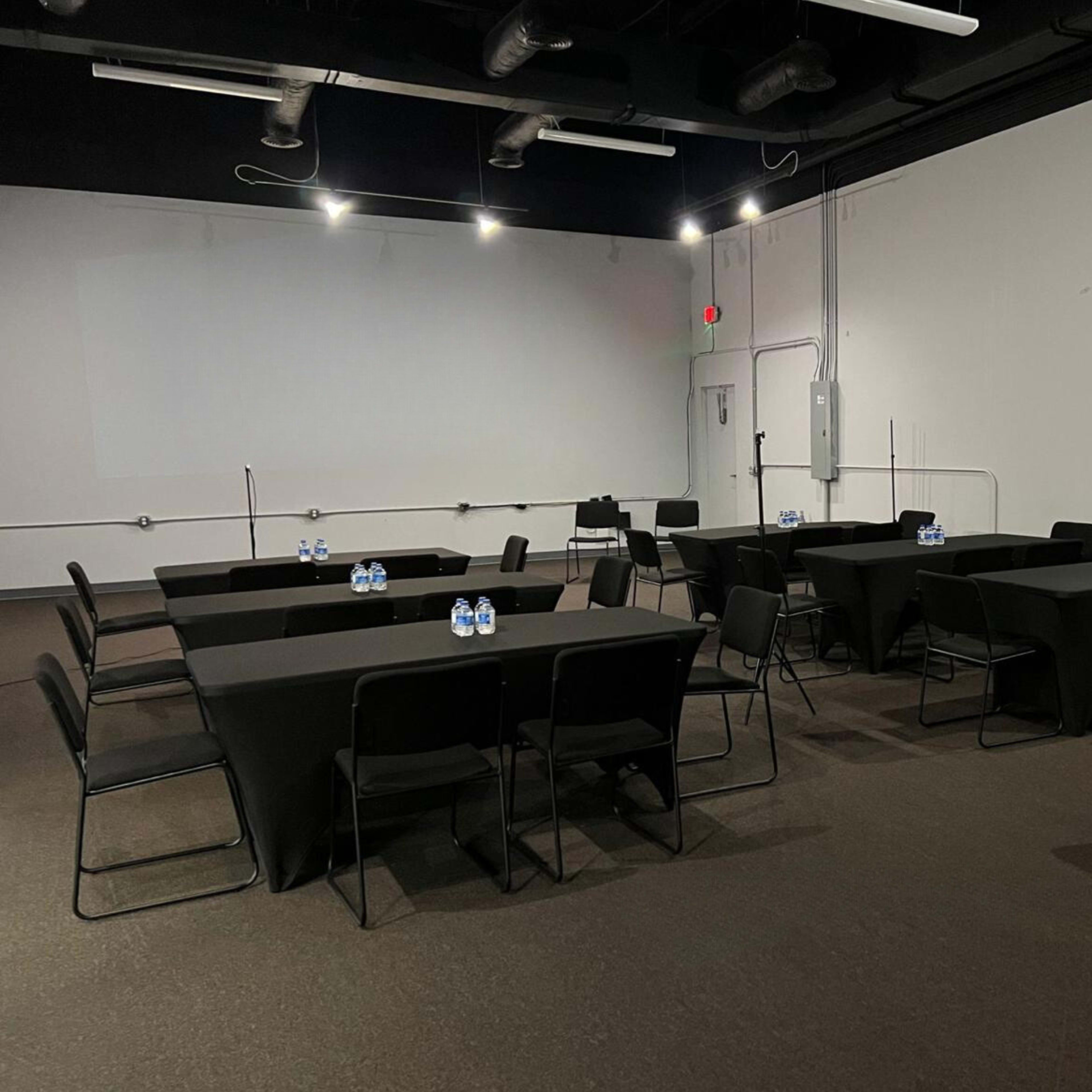 A minimalistic meeting room with several black-covered tables arranged in a rectangular formation, each with a bottle of water on top.