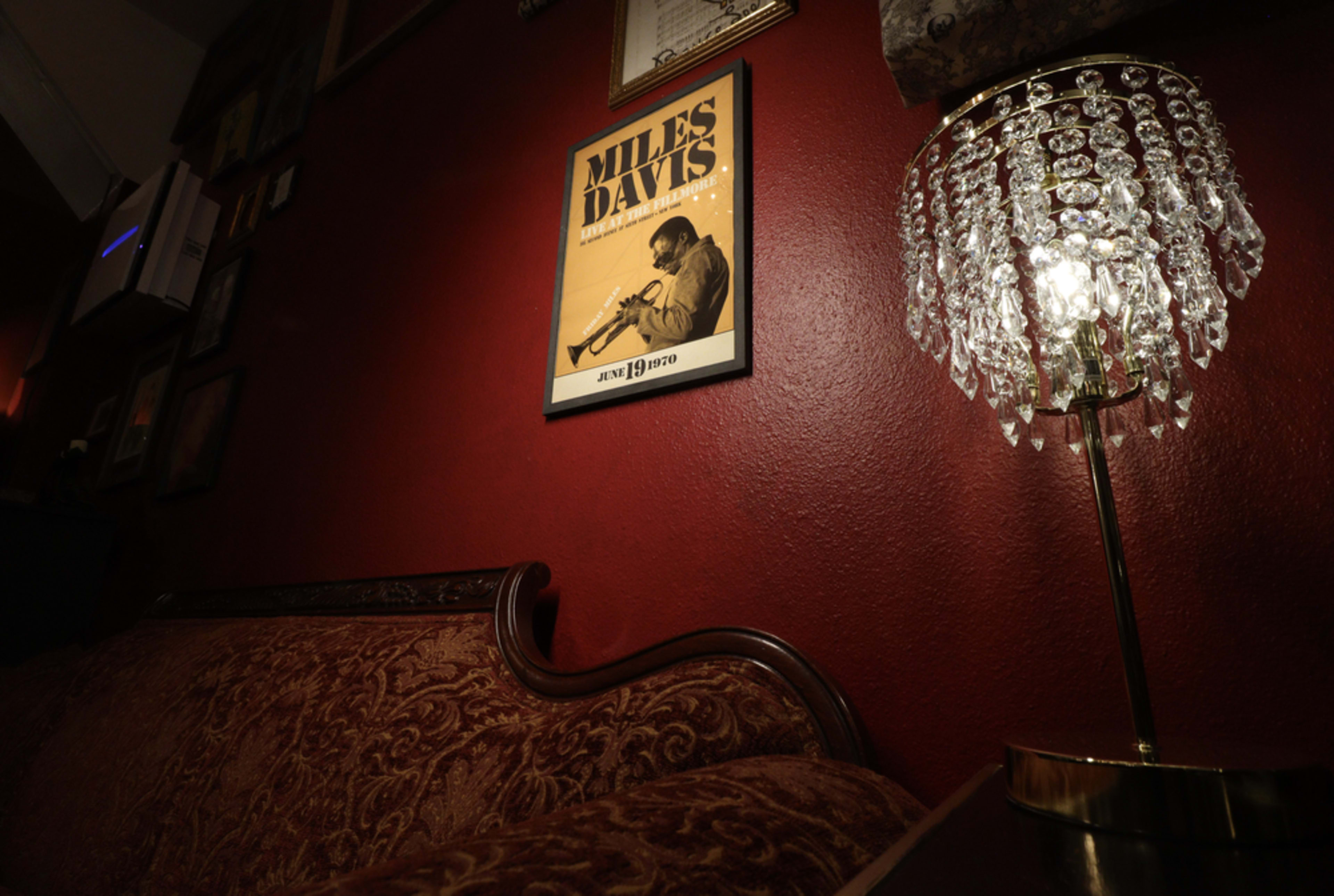 A velvet couch sits beneath a framed poster of Miles Davis on a red wall, alongside a decorative crystal lamp emitting warm light.