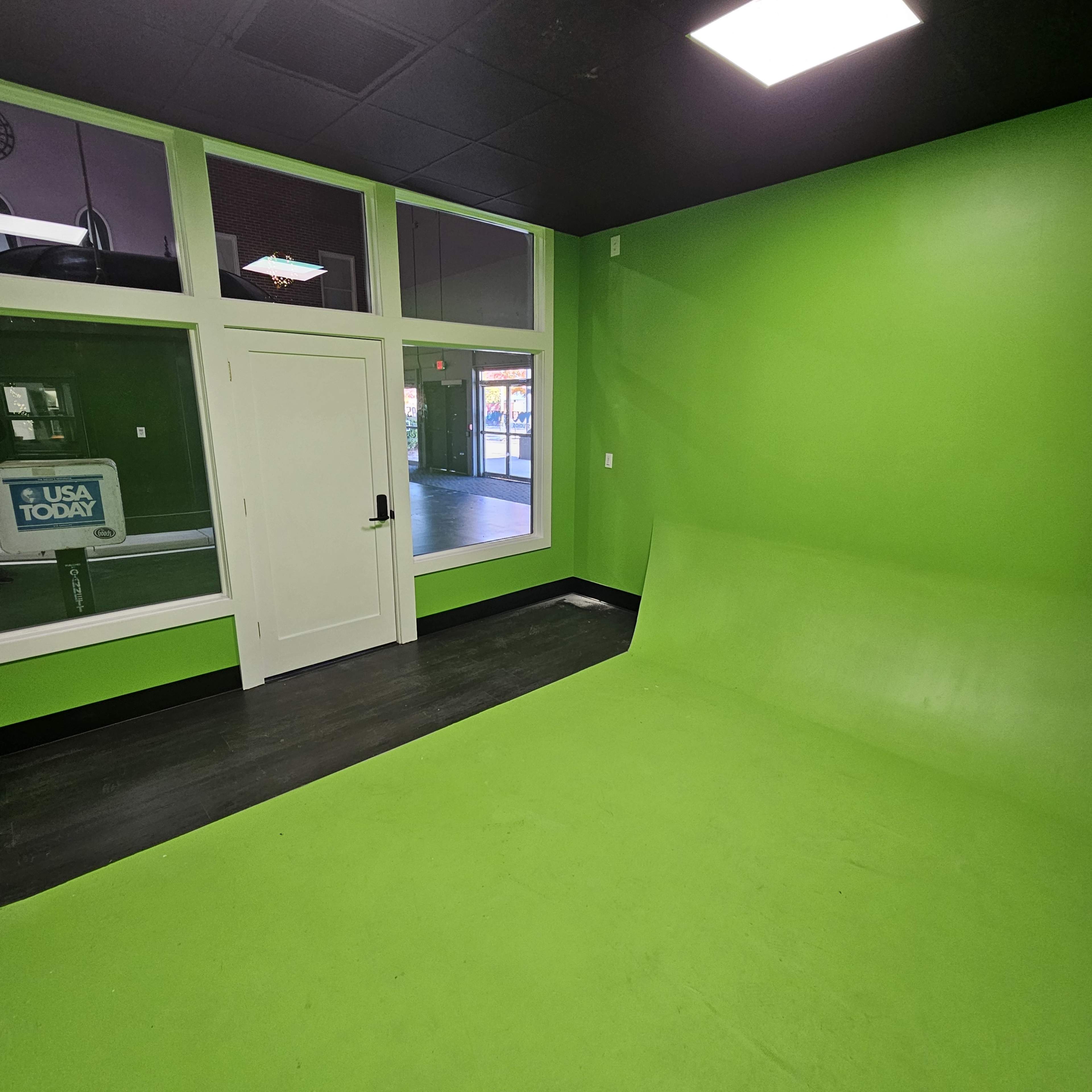 The image shows a bright green room with a smooth floor and wall, featuring a door and large windows that allow natural light to enter.