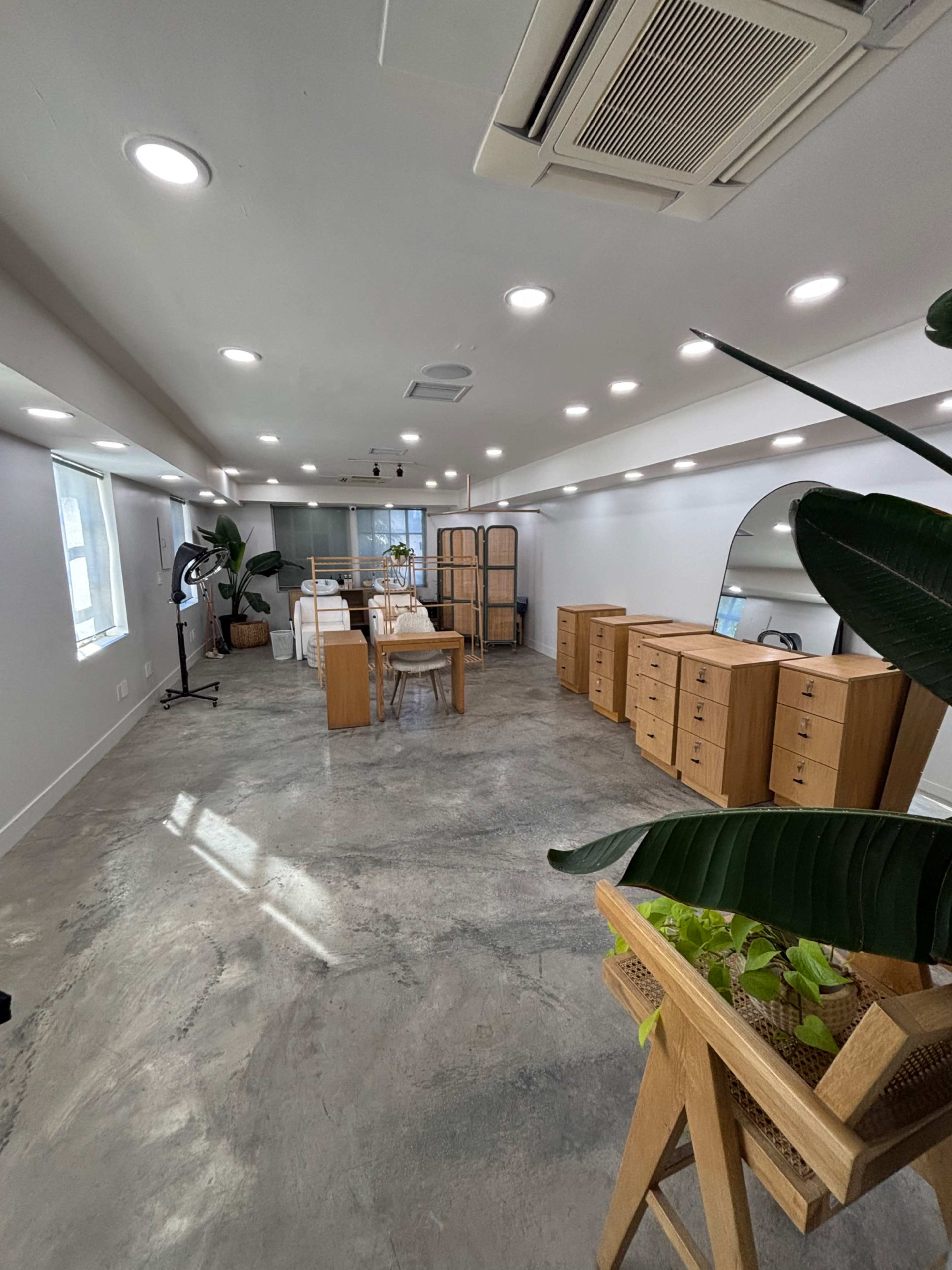 The image shows a spacious, well-lit office with wooden furniture, including tables and cabinets, set against a concrete floor.