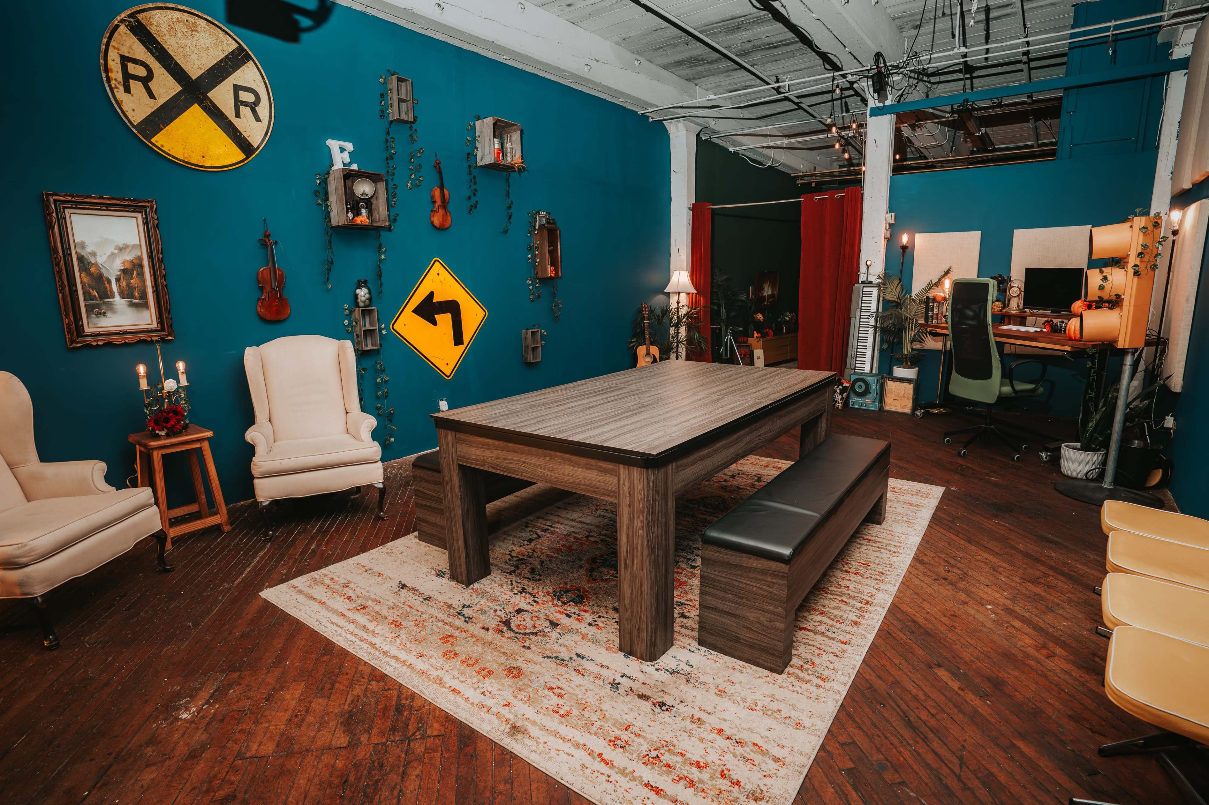A spacious room with a central wooden table surrounded by benches, decorated with various musical instruments, wall art, and traffic signs against a vibrant blue background.