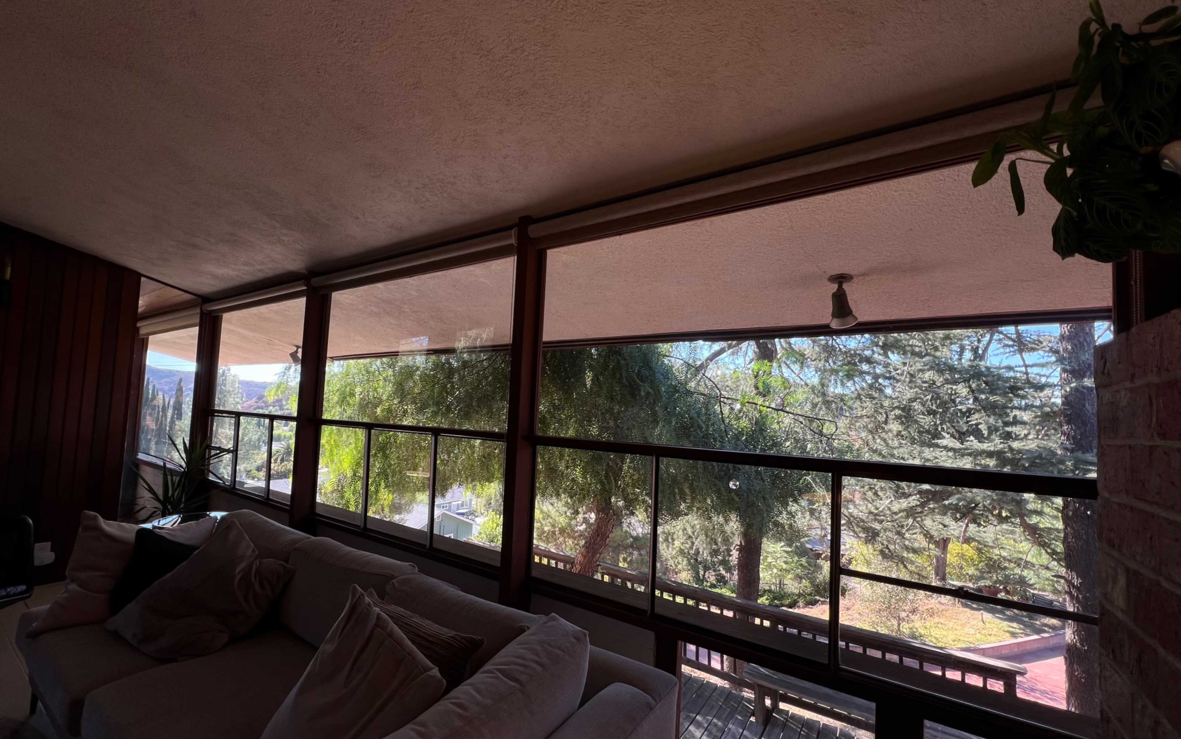 A couch is positioned in front of large windows that overlook a green landscape with trees on a sunny day.