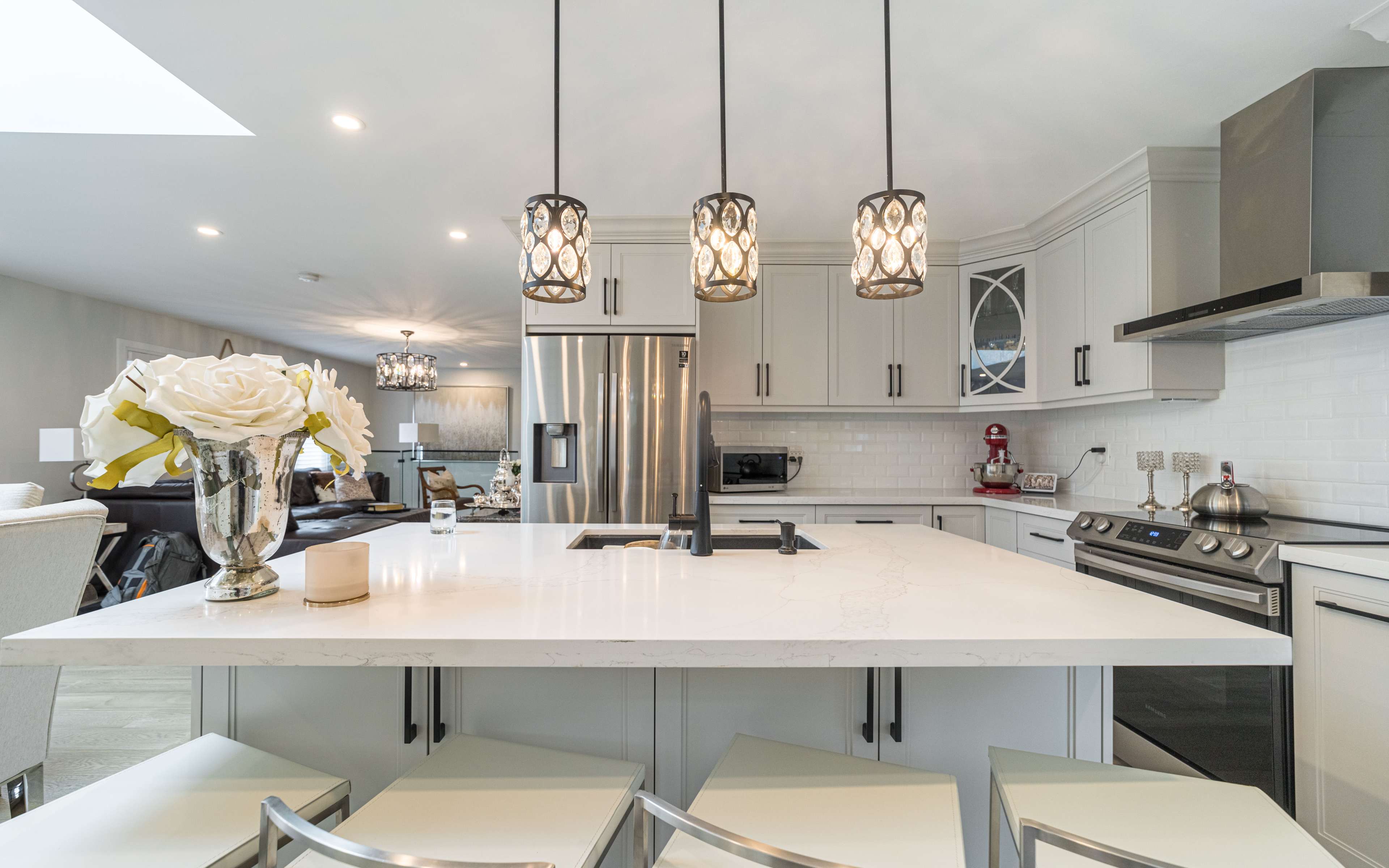 A modern kitchen features a large island with a white countertop, three pendant lights above, stainless steel appliances, and cabinetry in light tones.