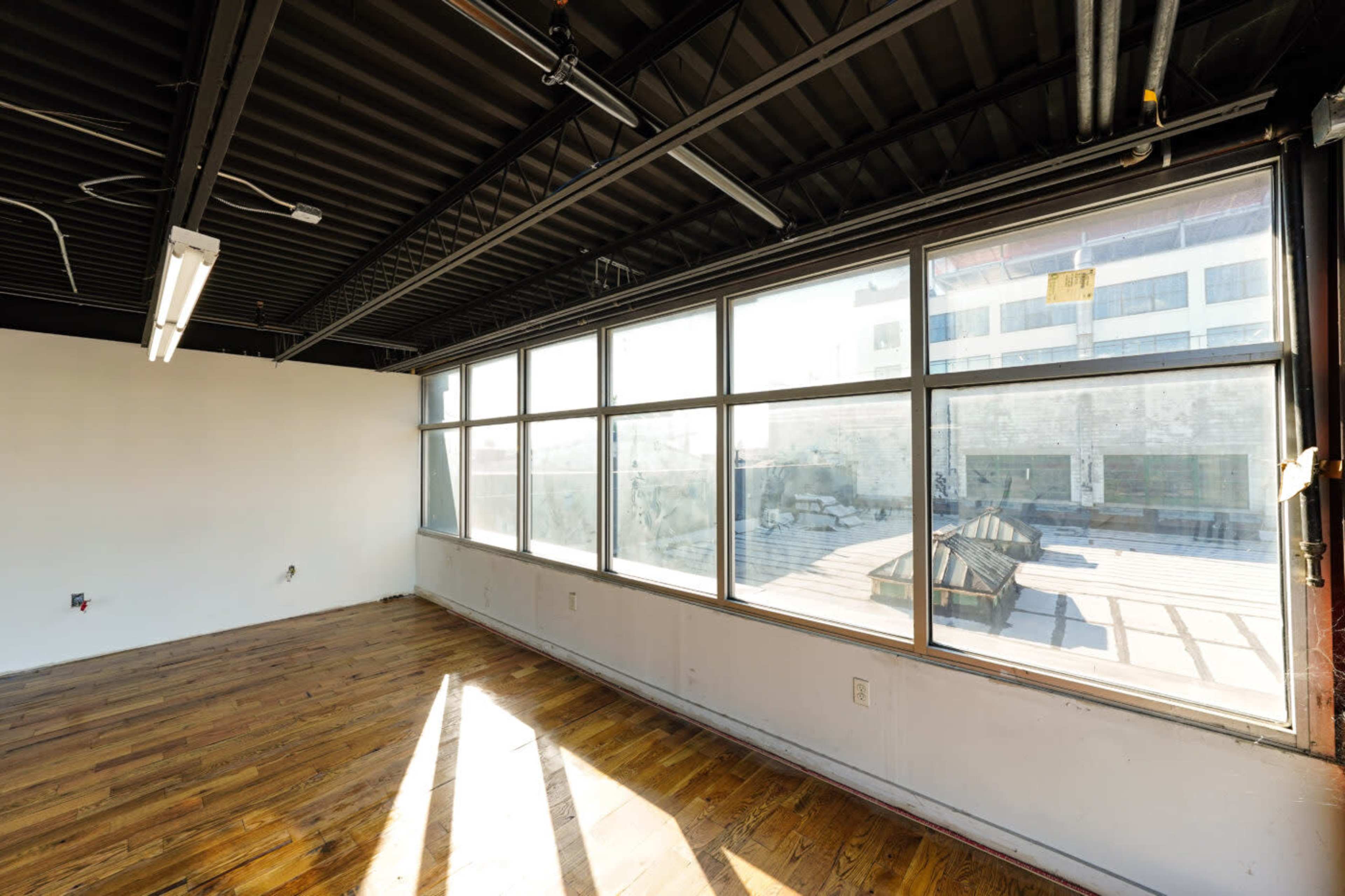 An empty room with large windows and wooden flooring, revealing a view of an outdoor space.