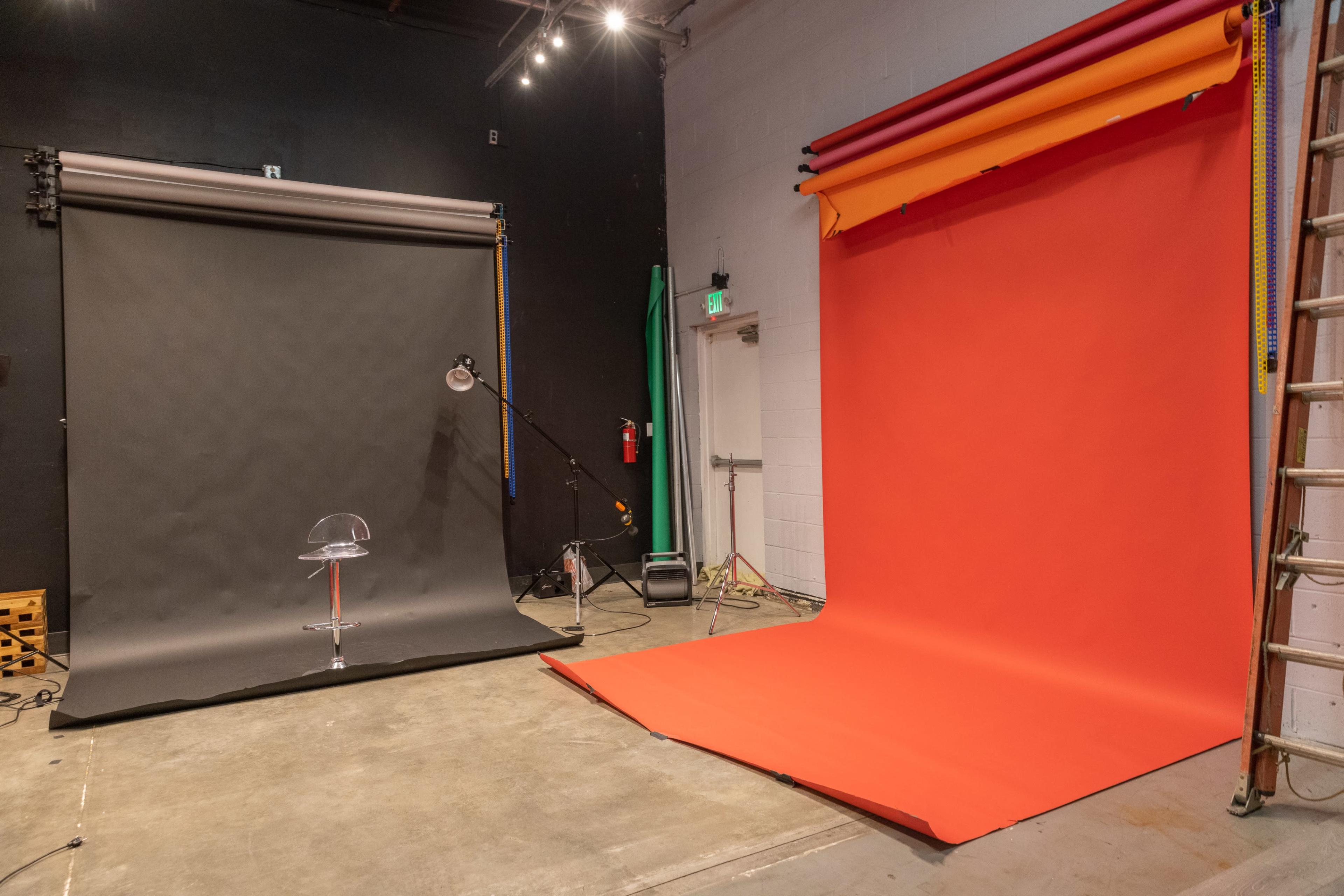 The image shows a photography studio with two backdrops, one black and one bright red, along with a clear chair and various equipment visible on the floor.