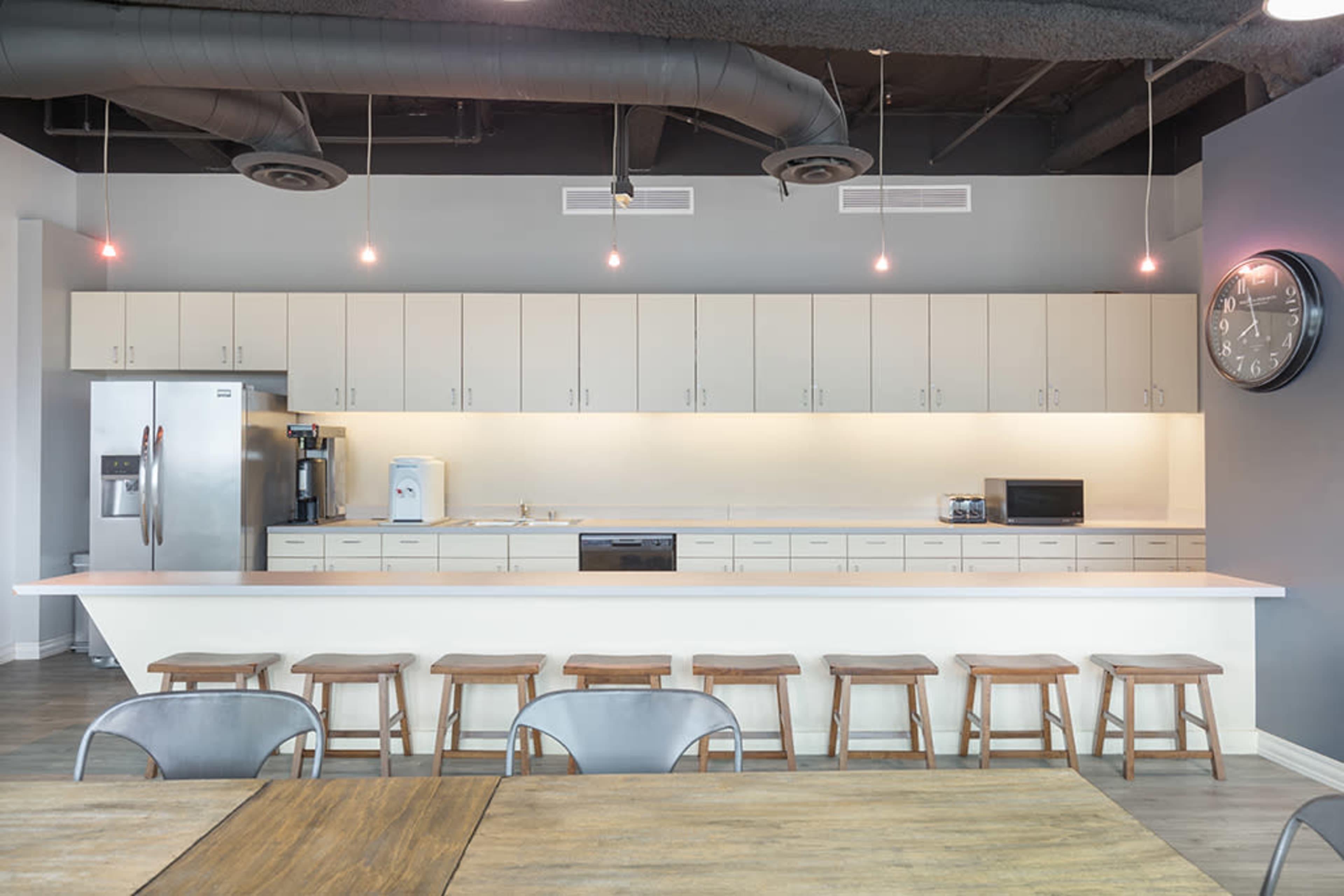 A modern kitchen area with a long countertop, several stools, and an array of cabinets above and below.