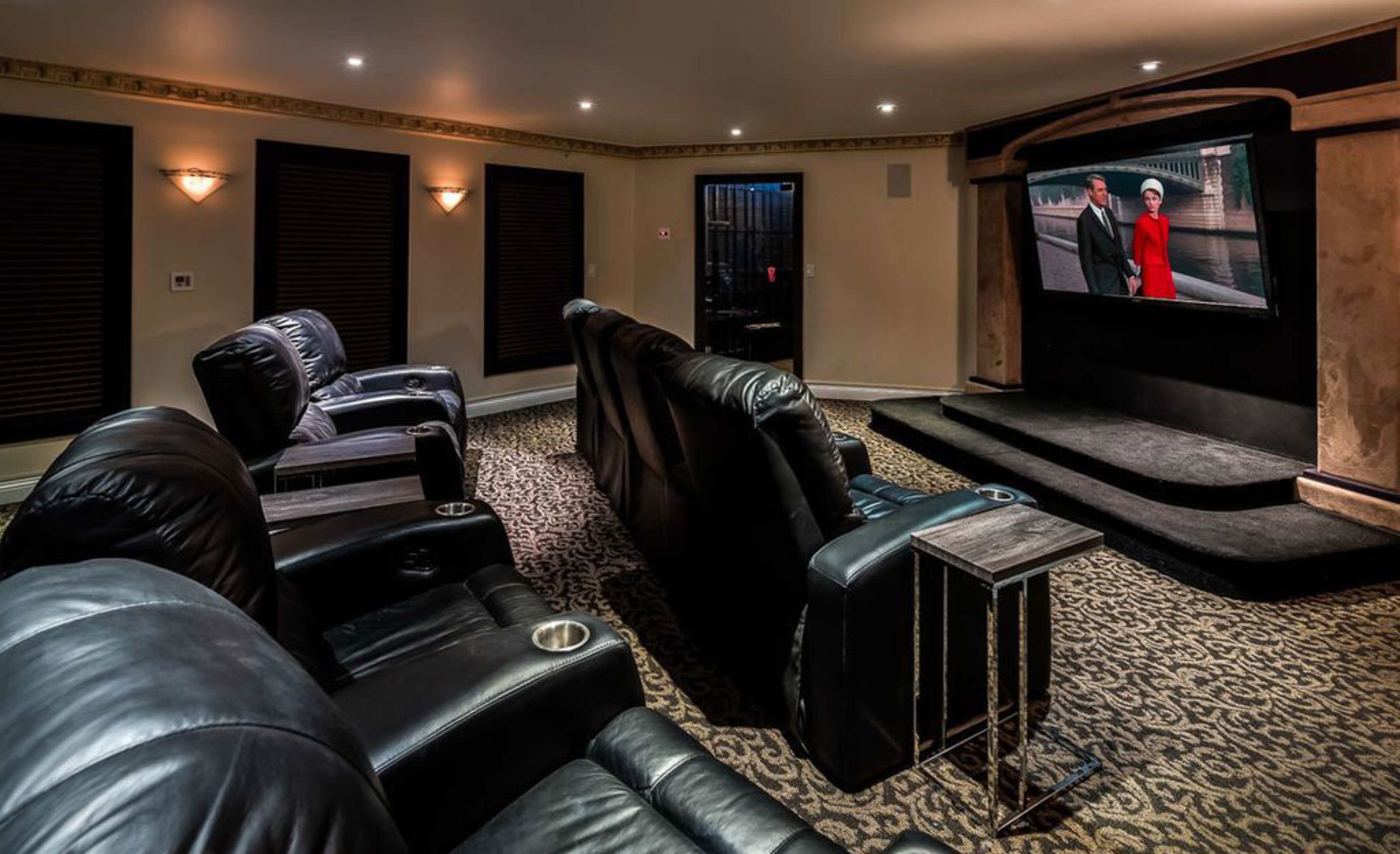 A dimly lit home theater featuring black leather recliners and a large screen displaying a movie.