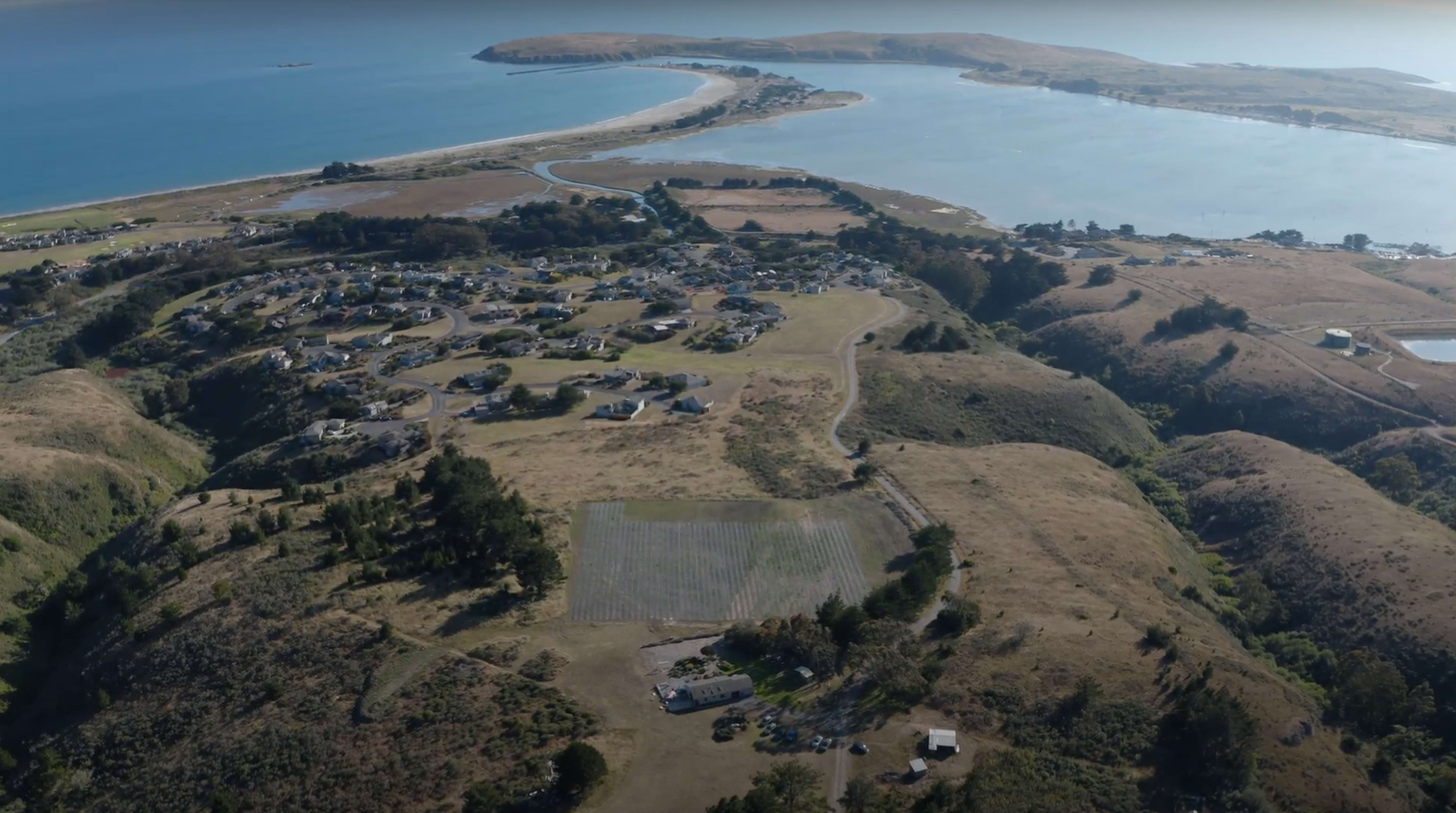 A coastal landscape with a winding river, residential areas, and rolling hills leading to the sea.