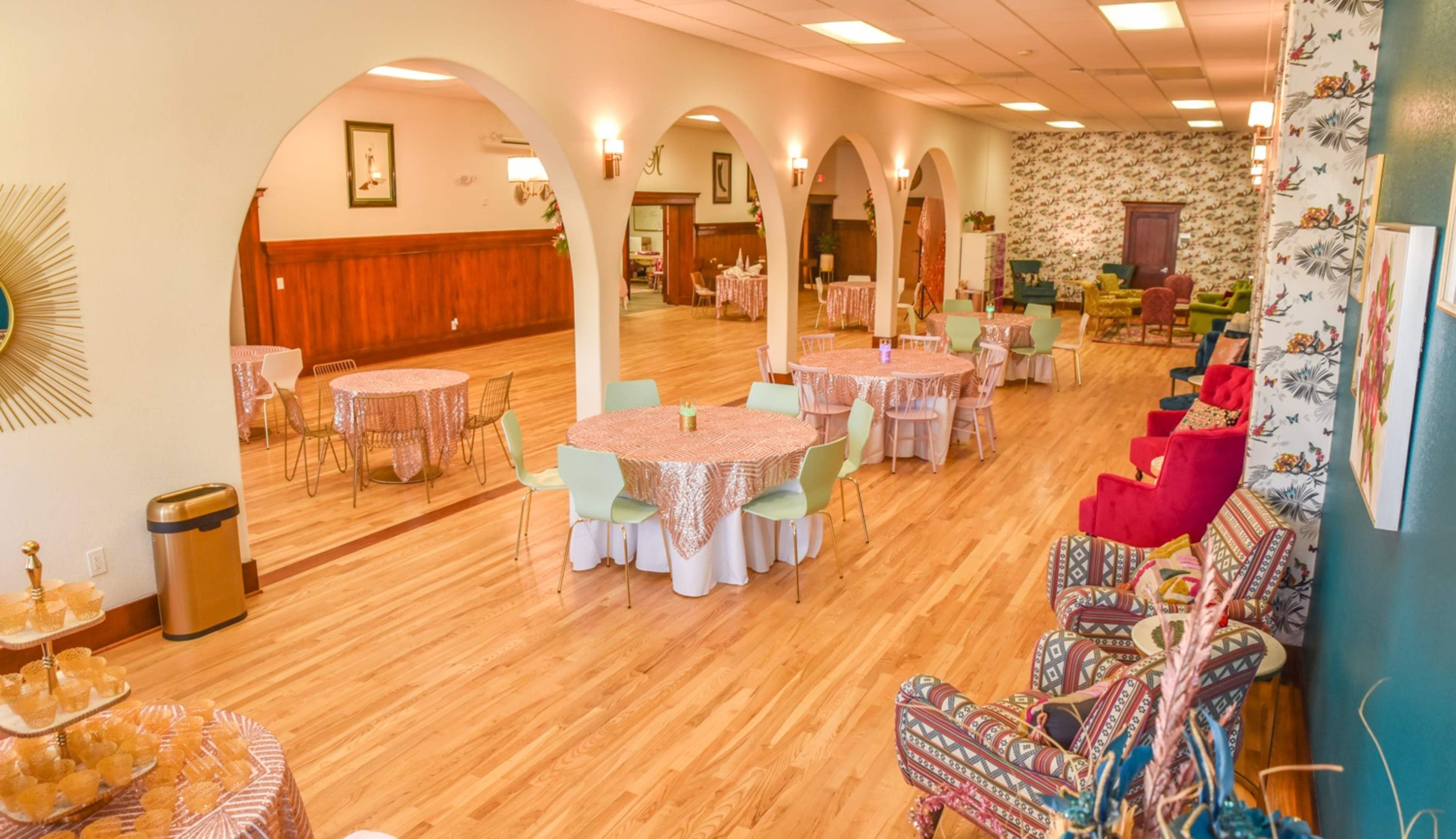 A spacious indoor event venue with round tables draped in patterned tablecloths, surrounded by colorful chairs and decorative walls.