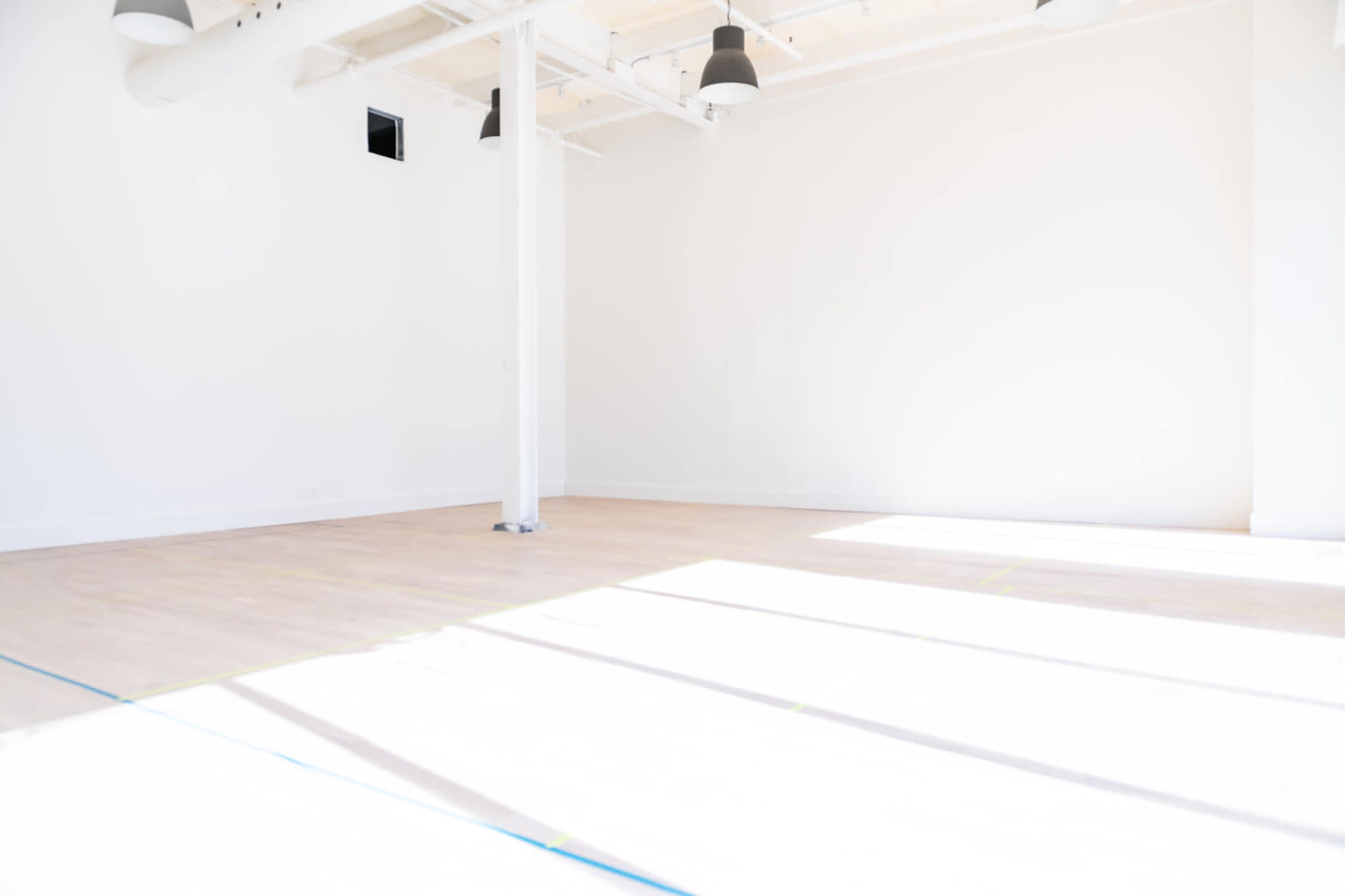 A spacious, well-lit room with wooden flooring and white walls, featuring a central support pole.