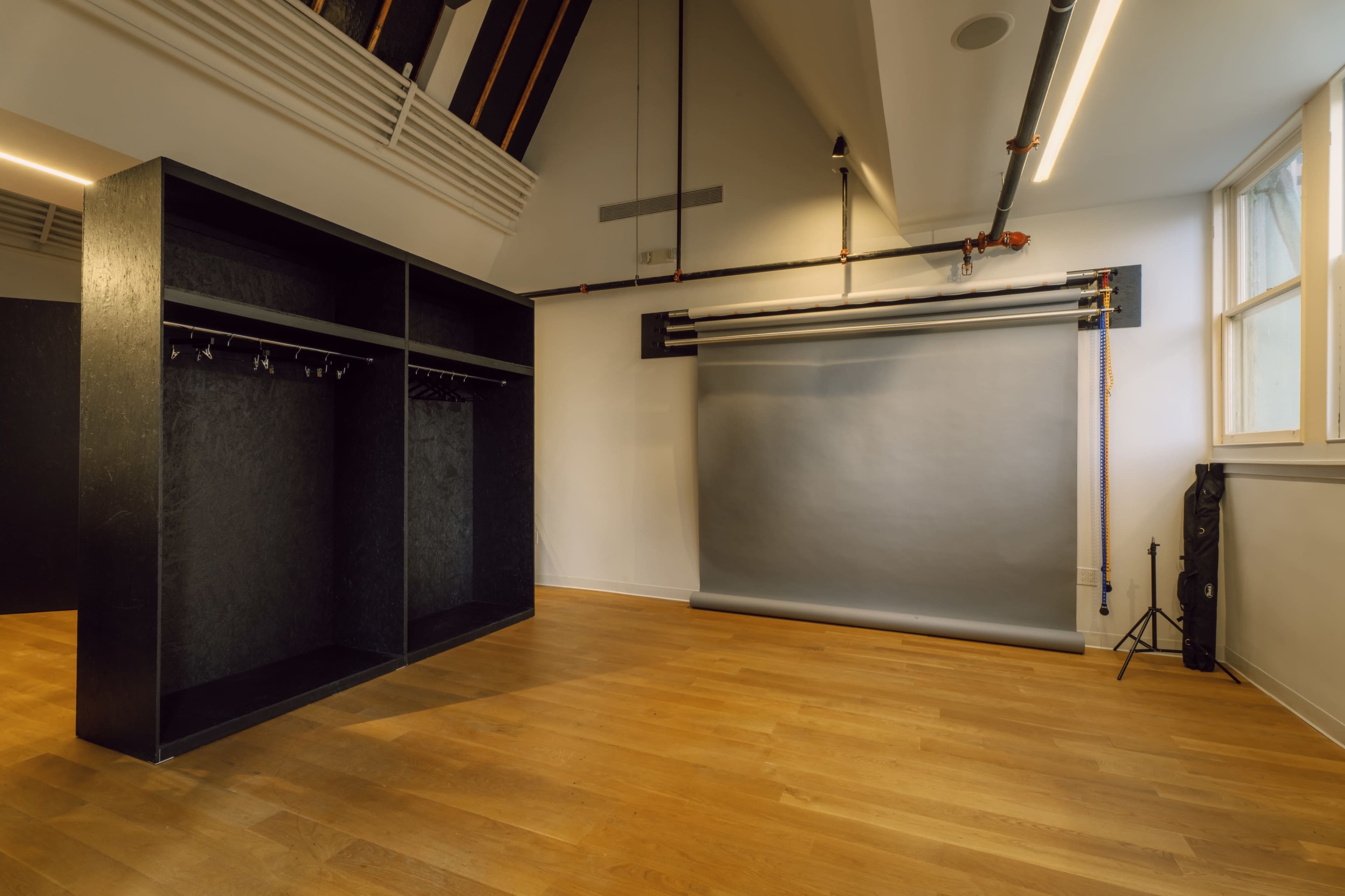 The image shows a spacious, well-lit photography studio featuring a large backdrop roll and a wardrobe area with hooks.