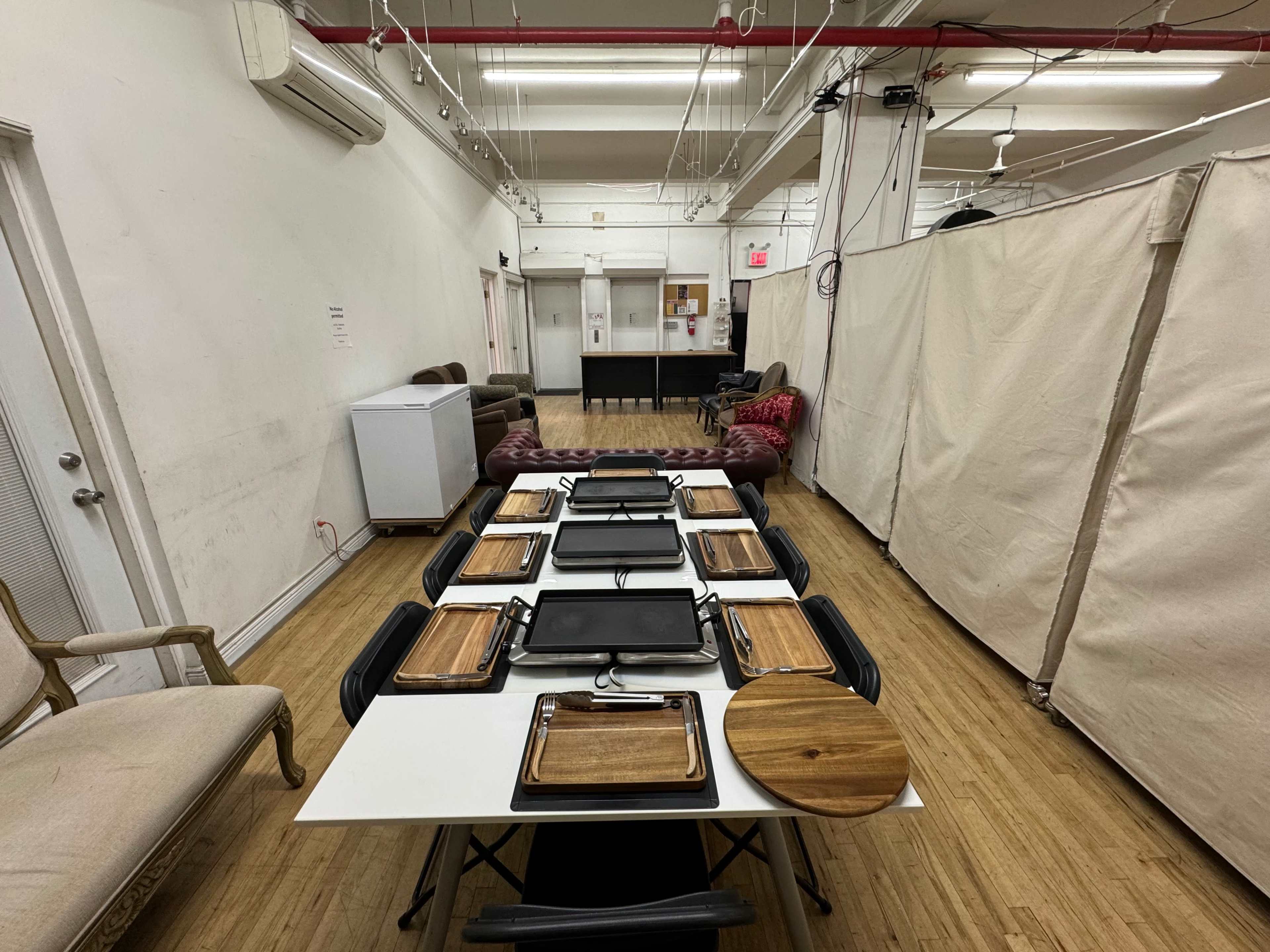 A long table is set up with several grilling trays and wooden serving platters in a spacious, minimalist room.