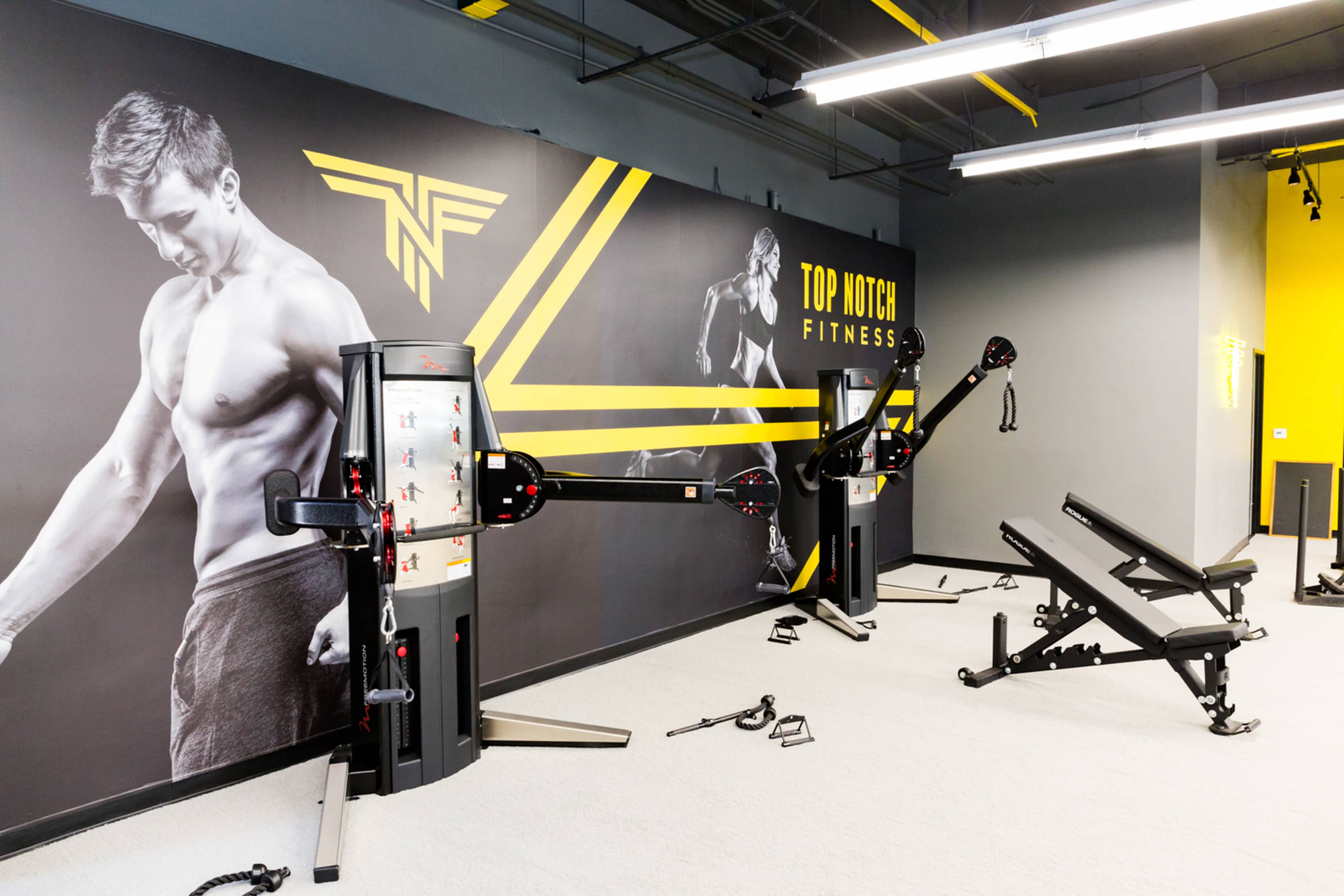 A fitness studio features workout machines and benches against a wall displaying a large mural promoting "Top Notch Fitness."