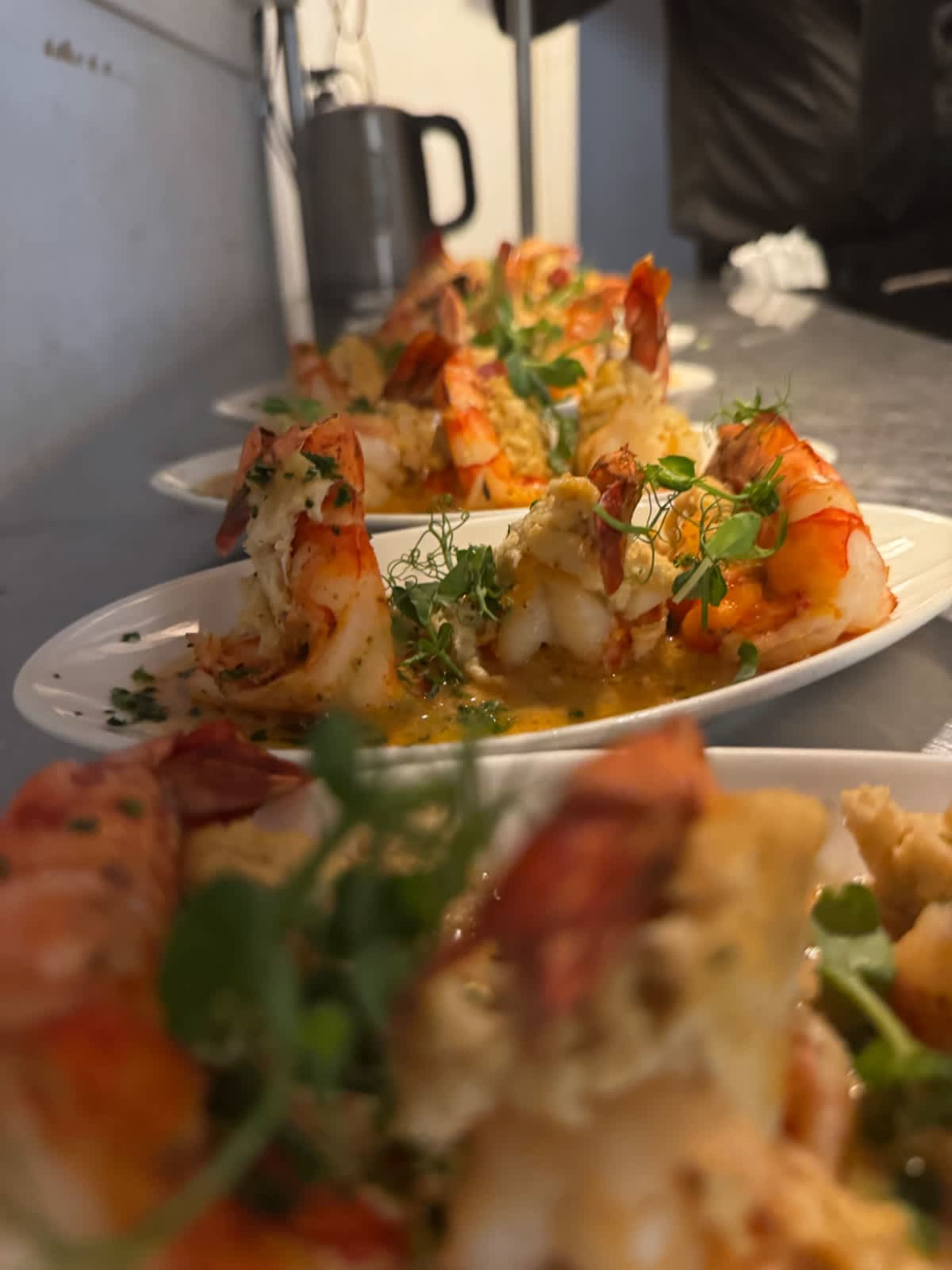 A row of plated shrimp dishes with garnishes is displayed on a countertop.