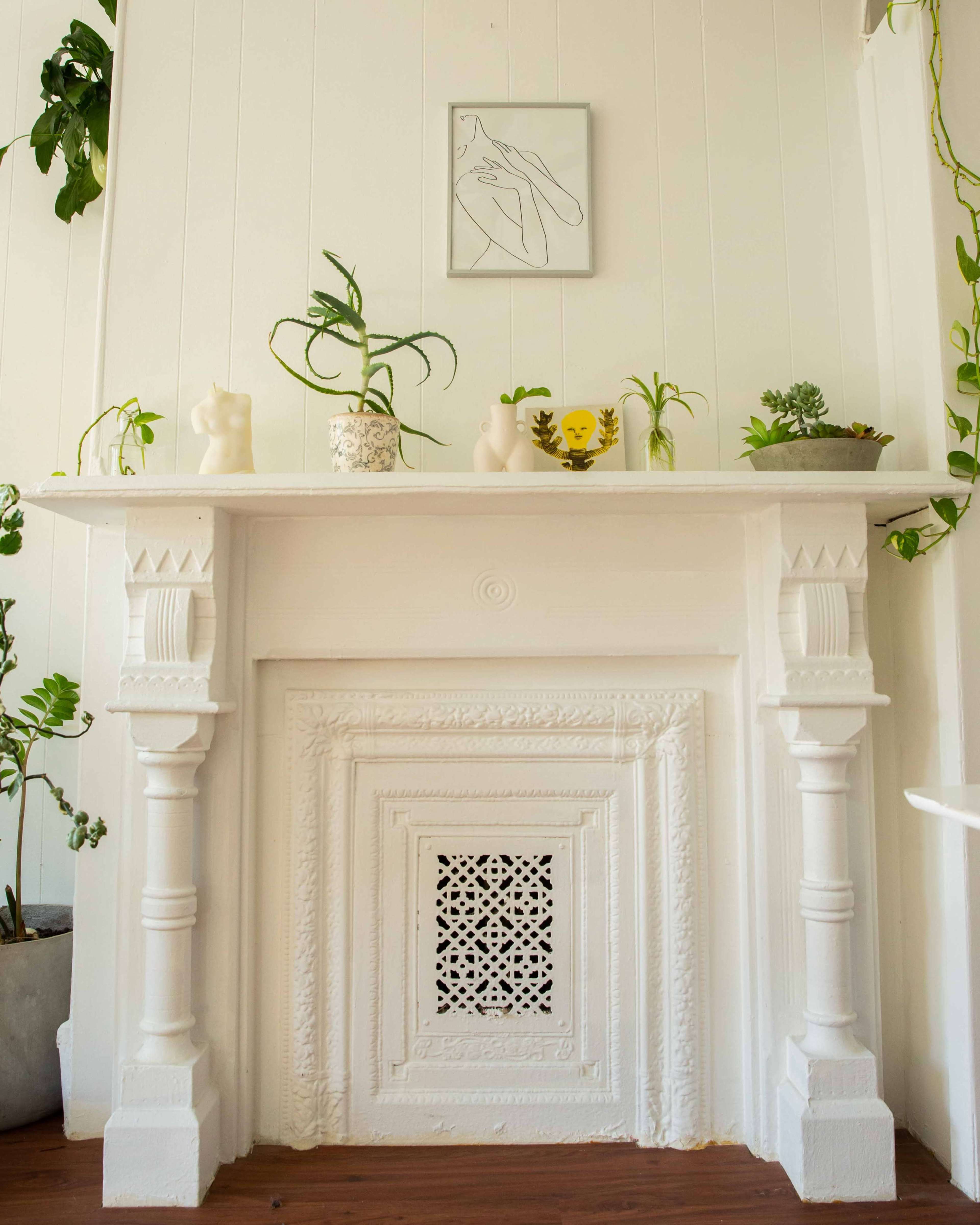 A white mantelpiece adorned with various plants and decorative items, set against a light-colored wall.