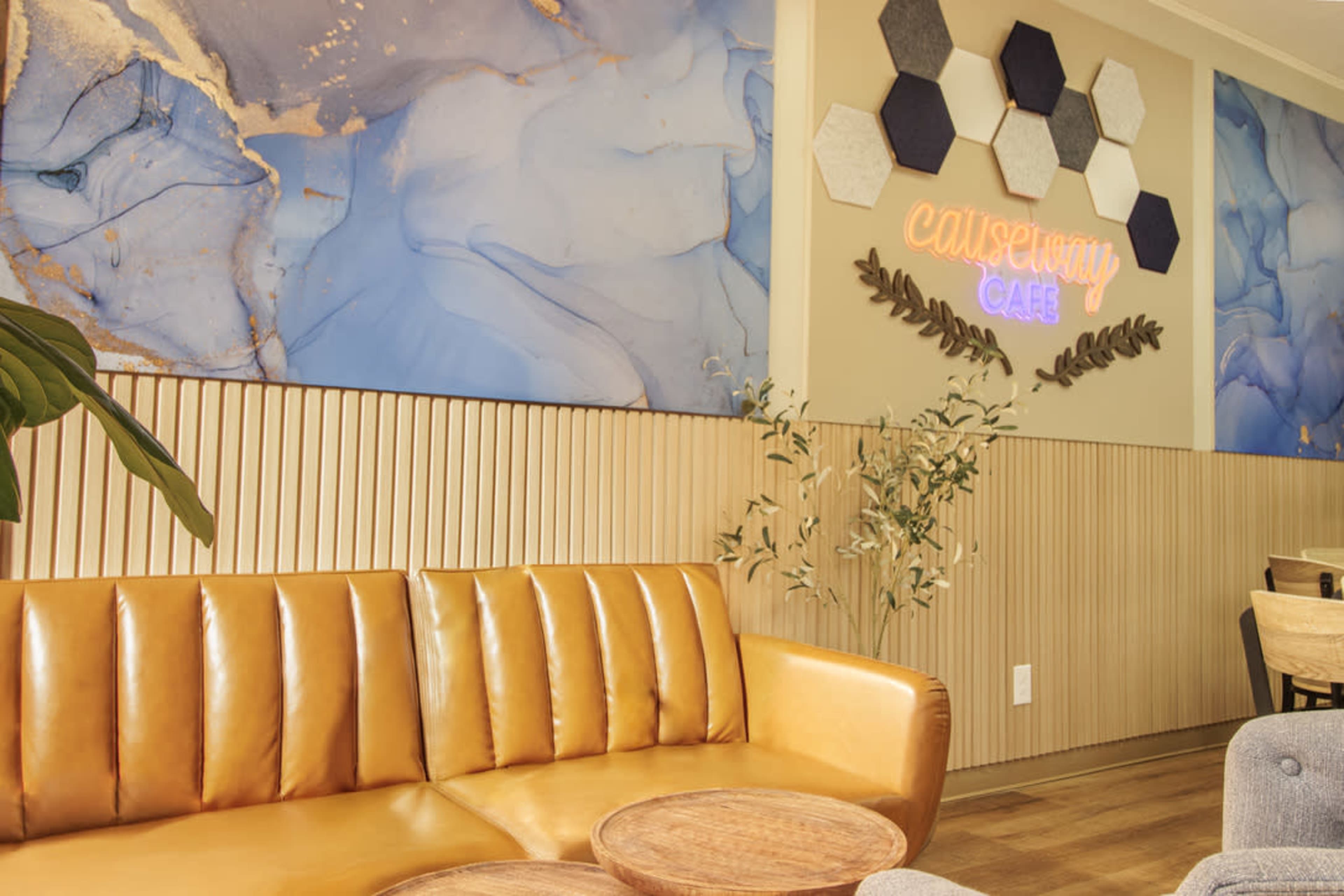 The image features a cozy café interior with a brown leather sofa, wooden tables, and a colorful abstract mural on the wall.
