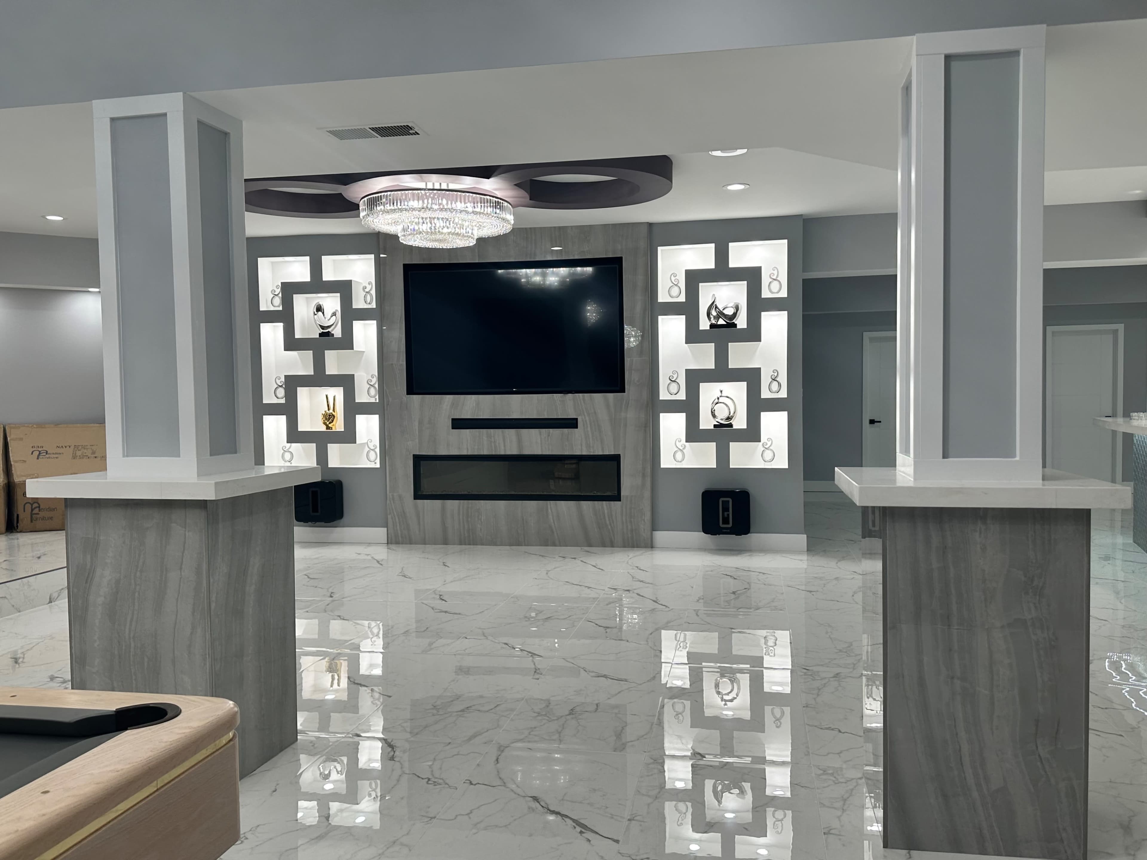 A modern living room featuring a large wall-mounted television, illuminated display shelves, and a sleek marble floor.