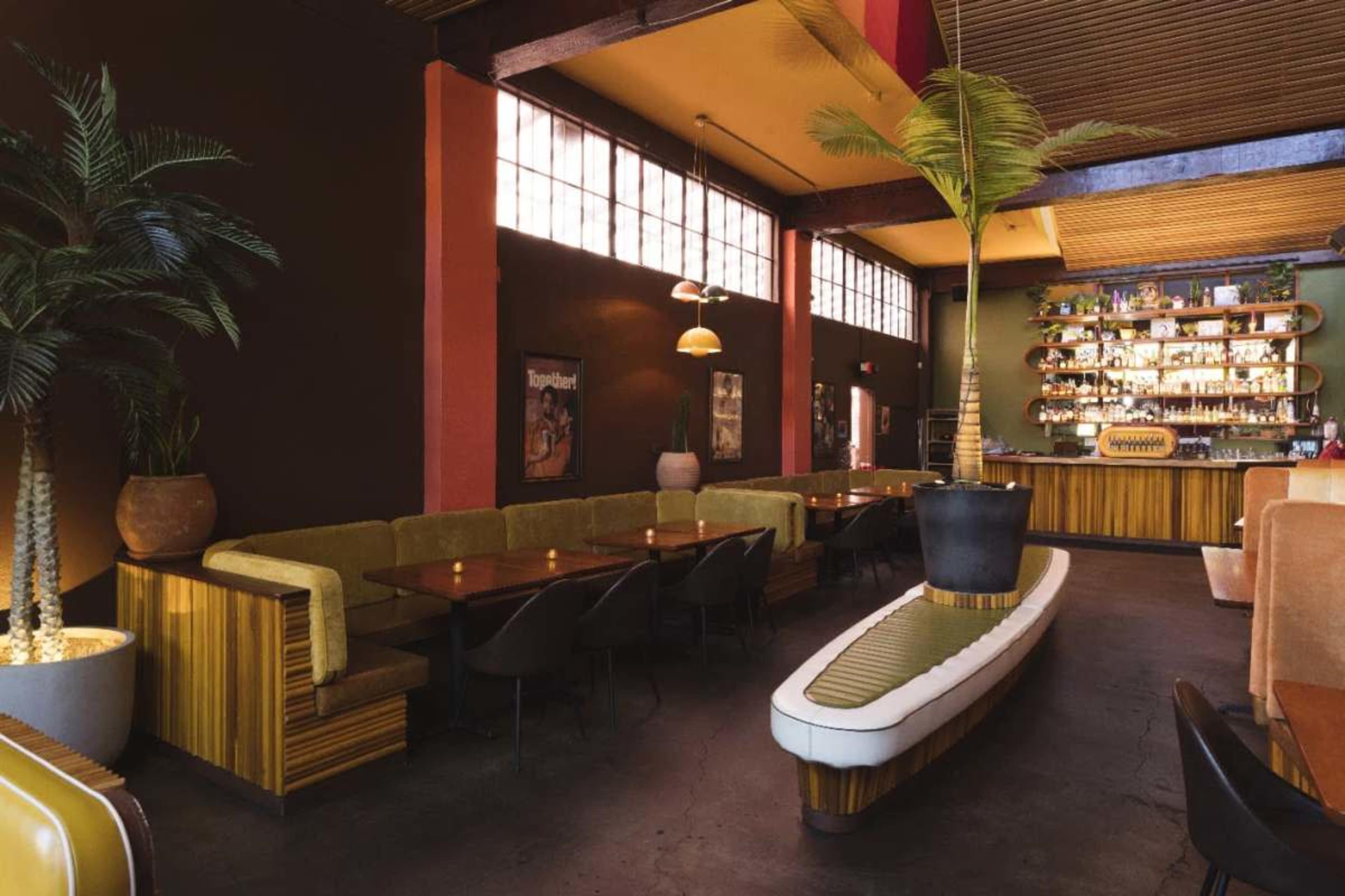 The image shows the interior of a restaurant featuring colorful walls, wooden furniture, and a long bar with shelves of liquor.