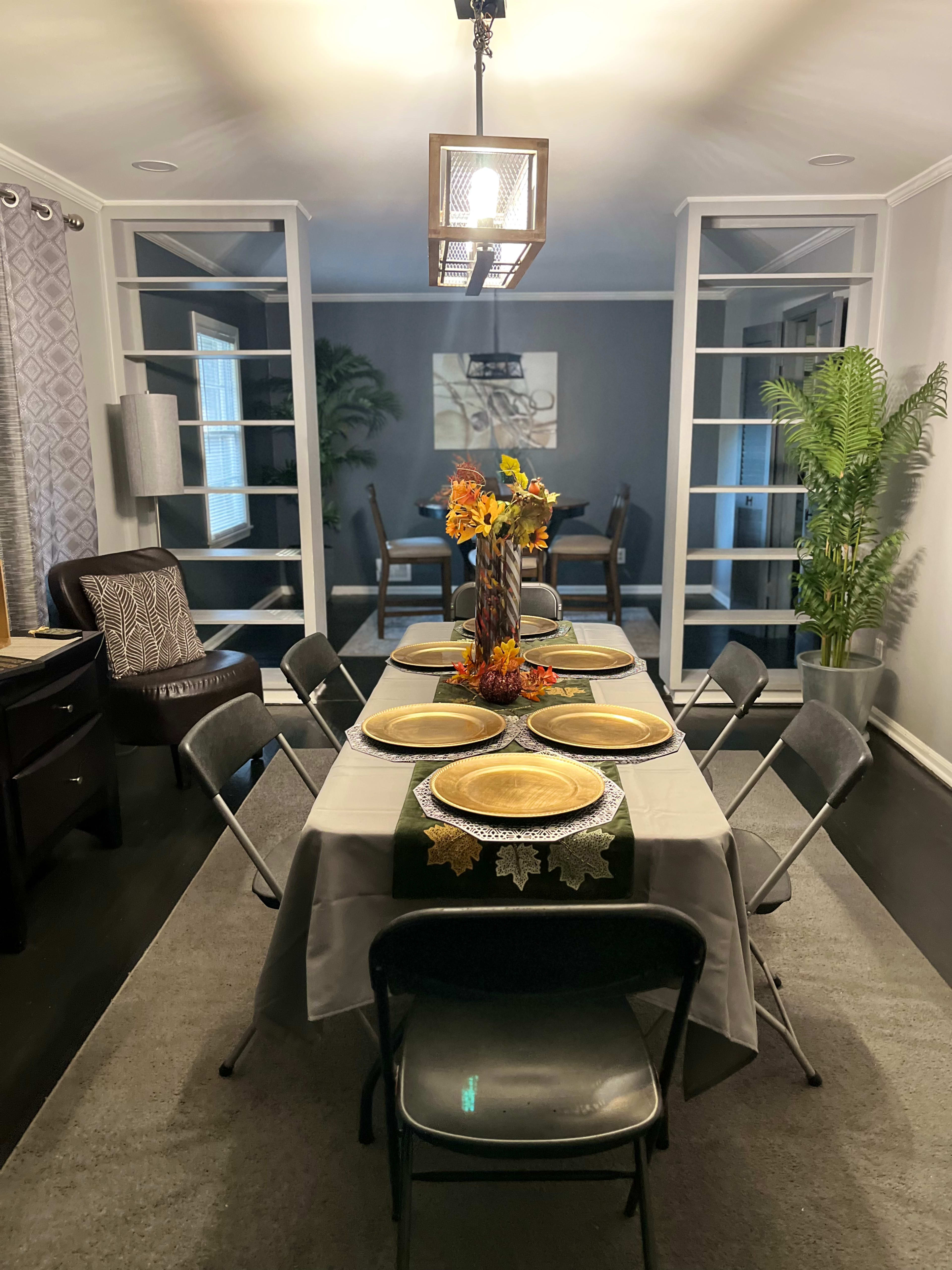 A dining room is set up with a large table adorned with plates and a centerpiece of autumn flowers.
