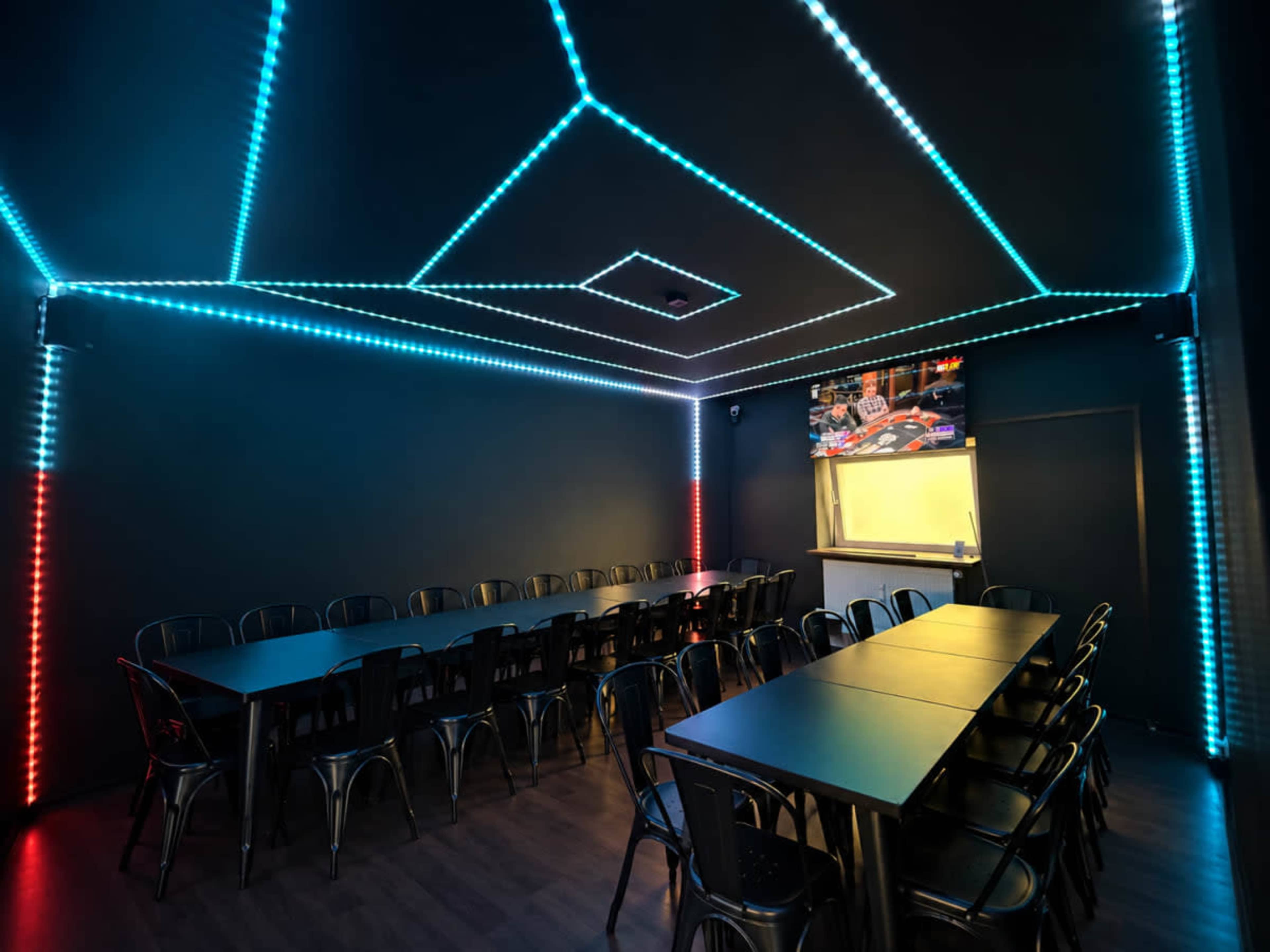 The image features a dark room with a long table and metal chairs, illuminated by blue and red LED lights along the ceiling.