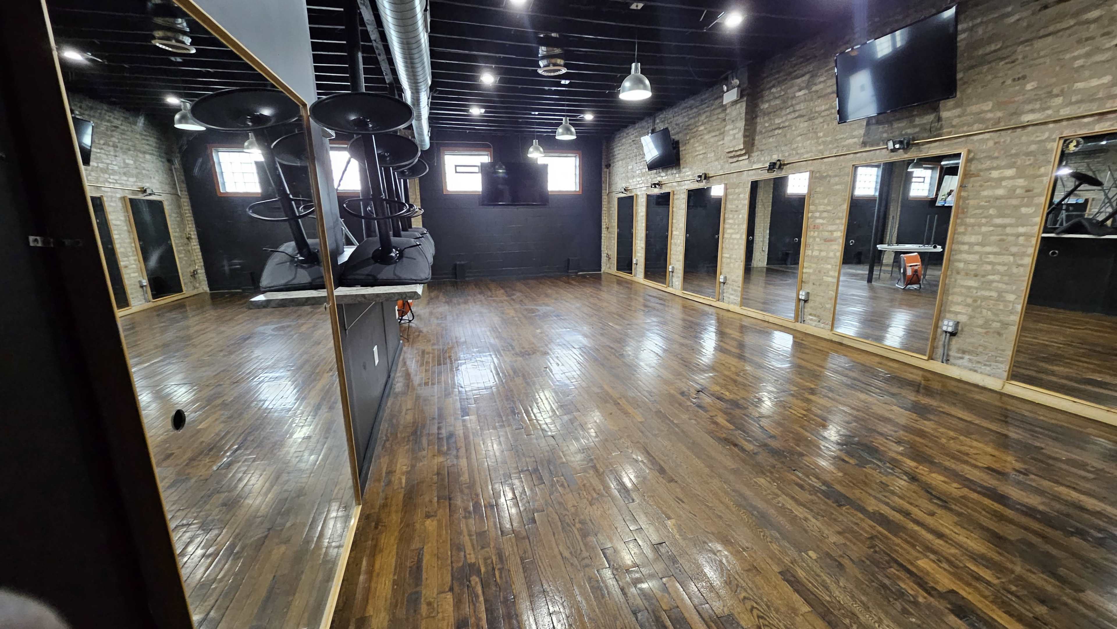 The image shows an empty fitness studio with polished wooden floors and large mirrors along the walls.