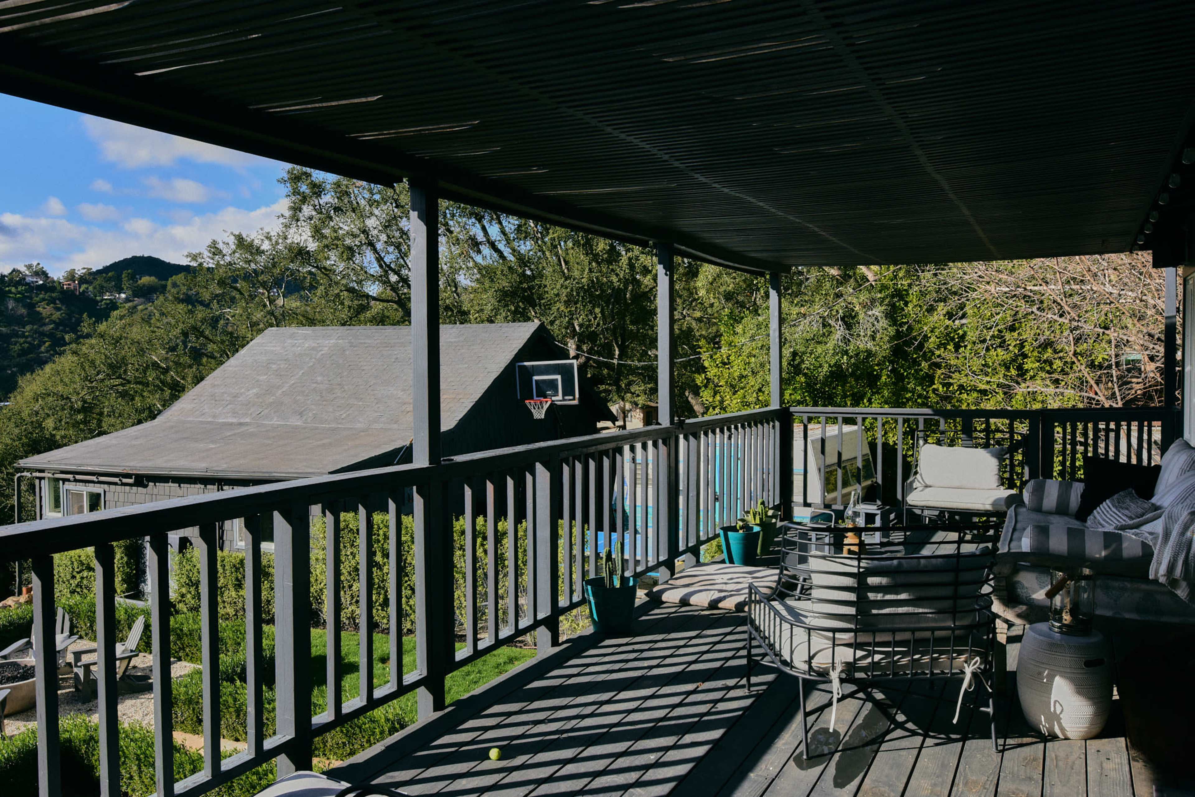 A covered porch with a railing overlooks a backyard that includes a basketball hoop and a shed.