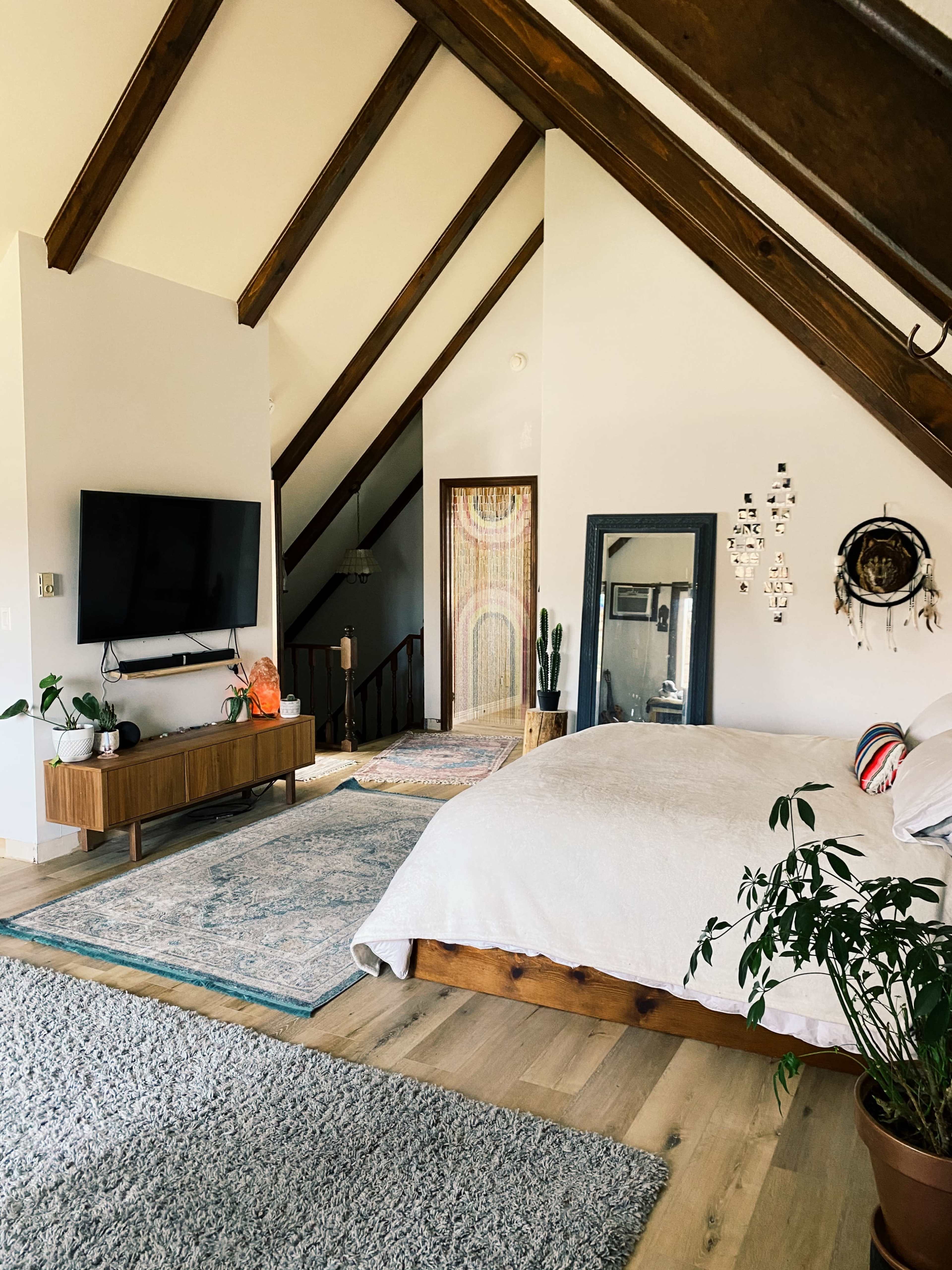 A spacious bedroom features a wooden bed, a large TV mounted on the wall, and a staircase leading to an upper level.