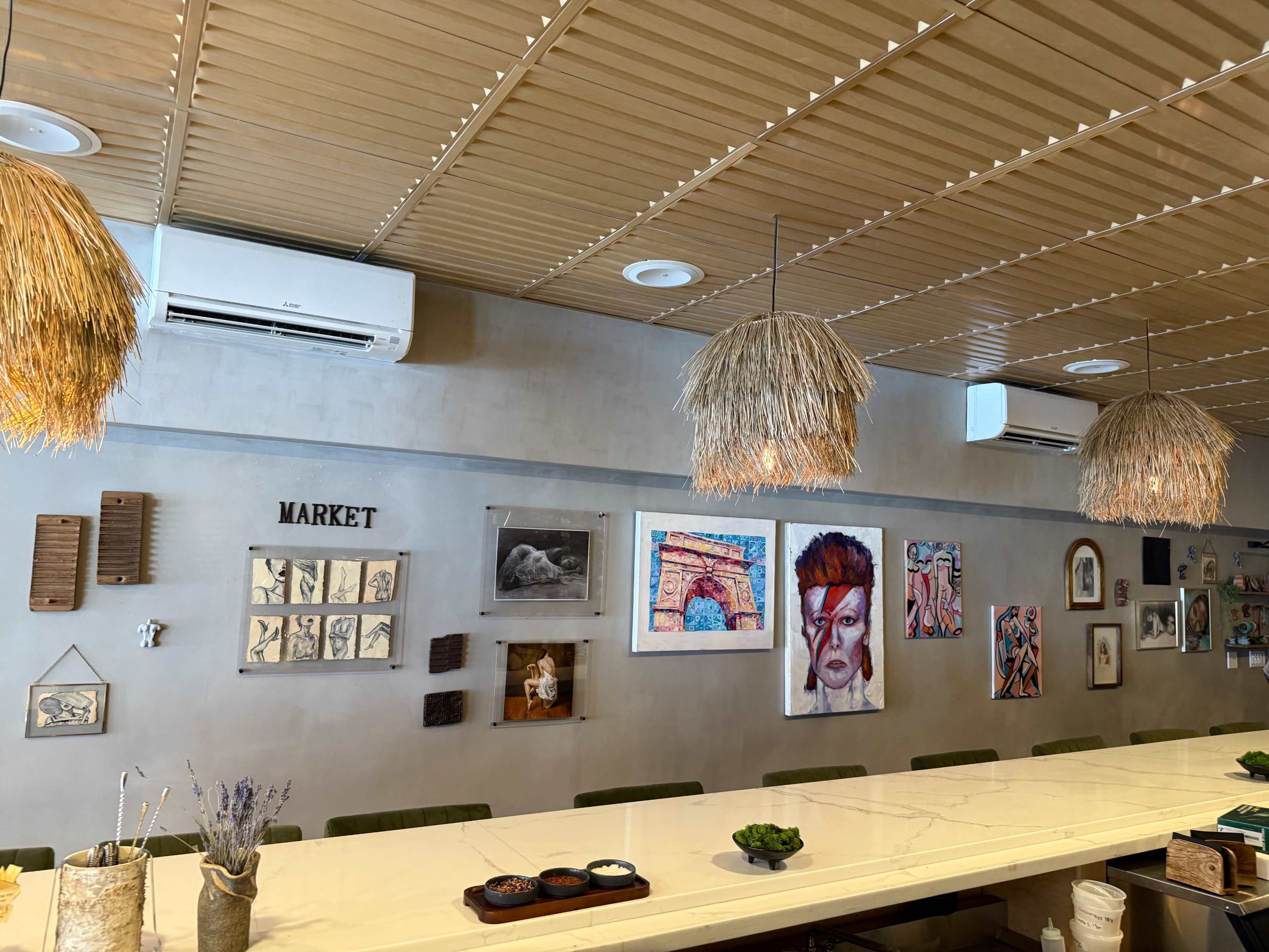 The scene features a dining area with a long white table, straw pendant lights, and a wall adorned with various artworks and decor items.