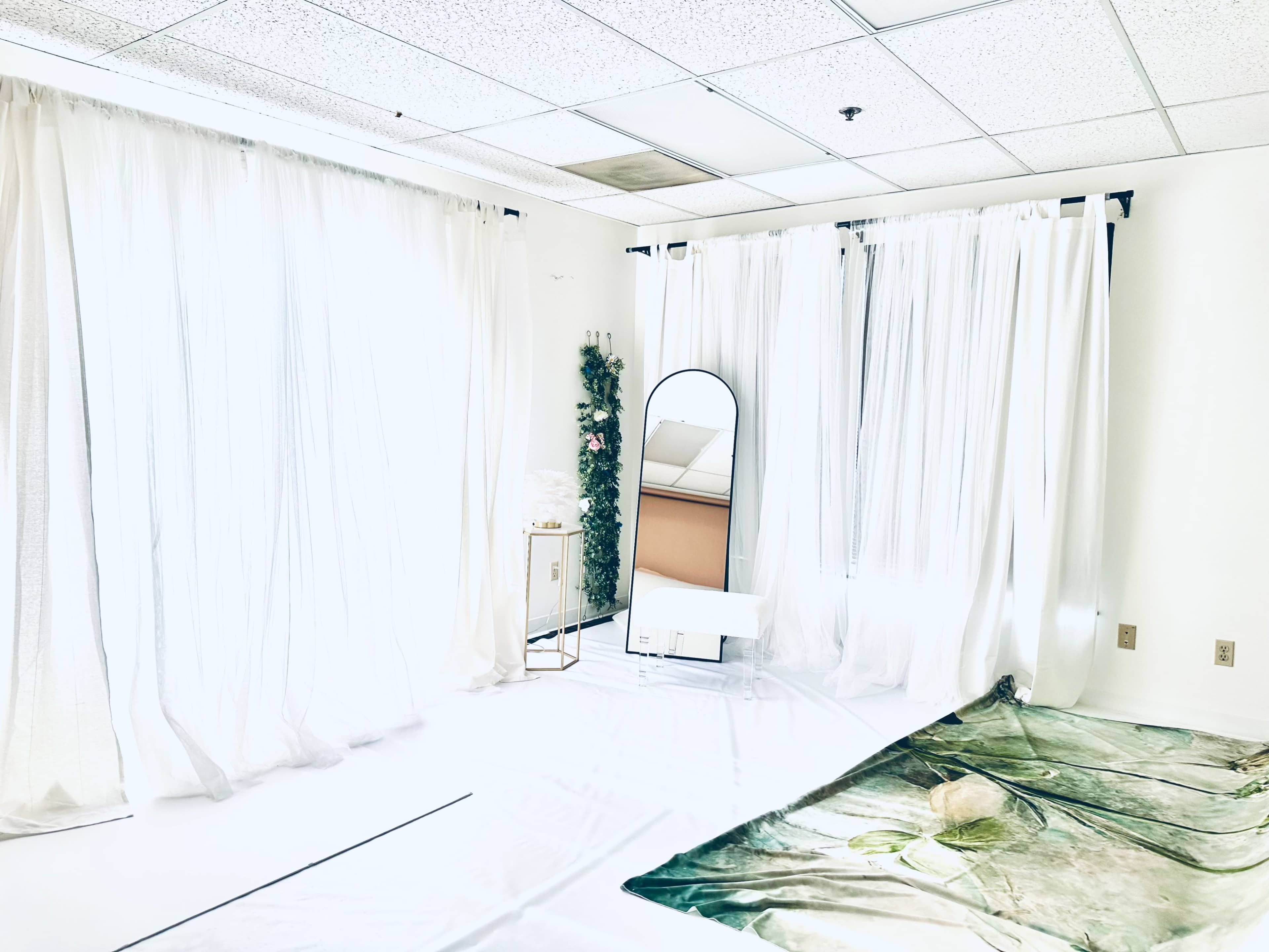 A bright, minimalist room with white curtains, a mirror, and a floor covering featuring a nature scene.