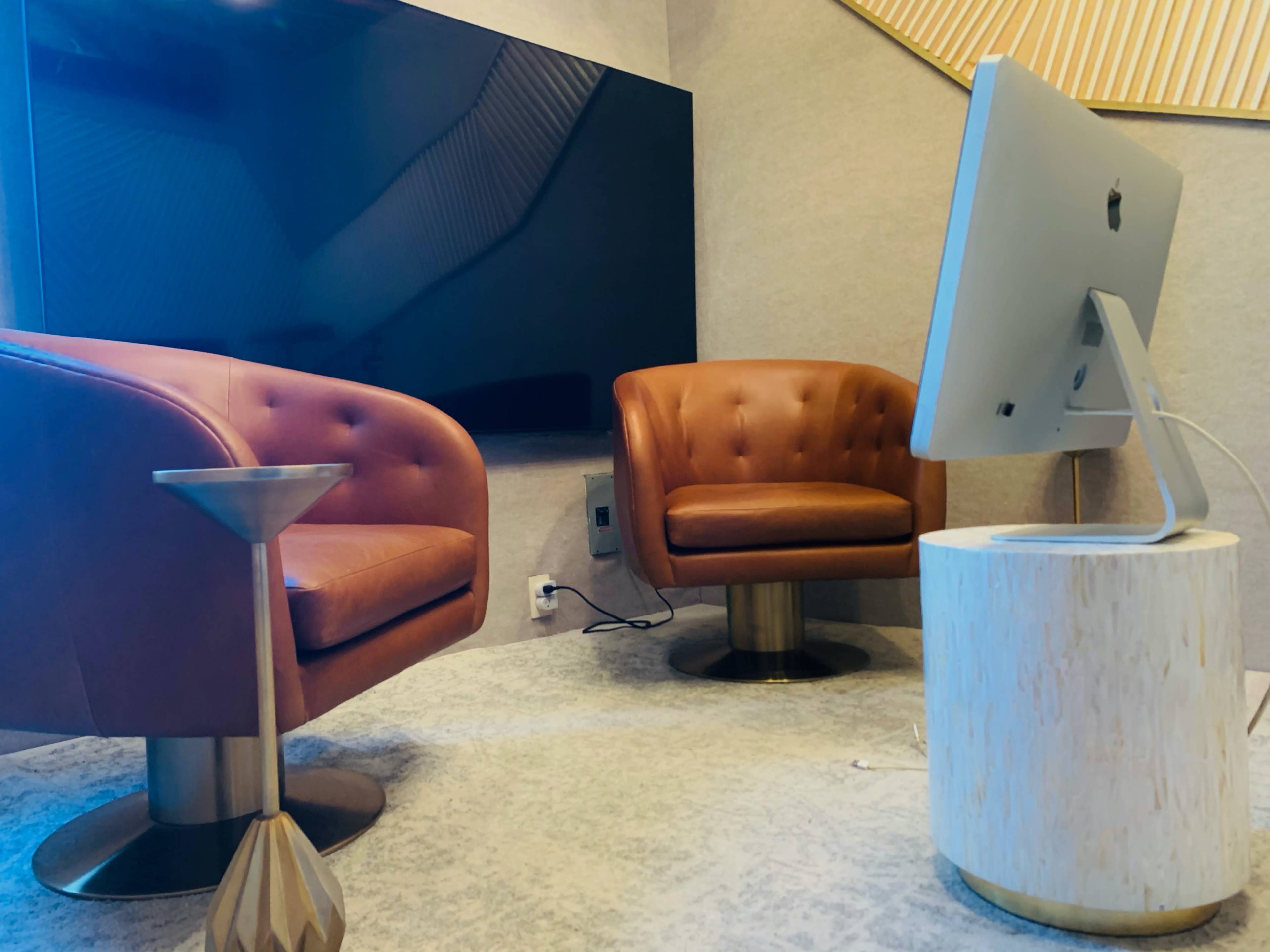 A modern meeting room featuring two brown leather chairs, a round white table, and a large television mounted on the wall.