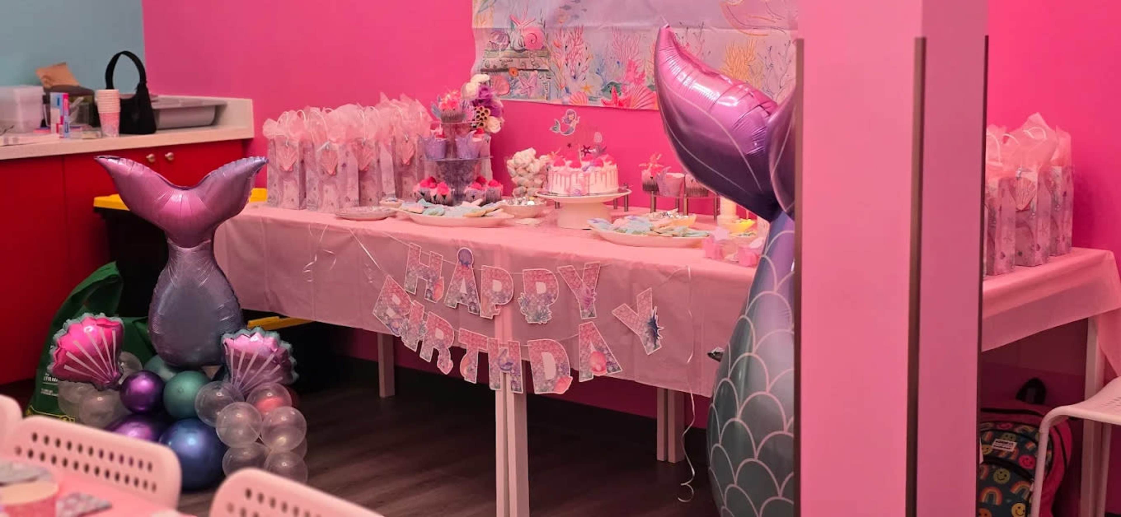 The image shows a colorful birthday party setup with a pink and purple theme, featuring a table decorated with sweets, balloons, and a "HAPPY BIRTHDAY" banner.