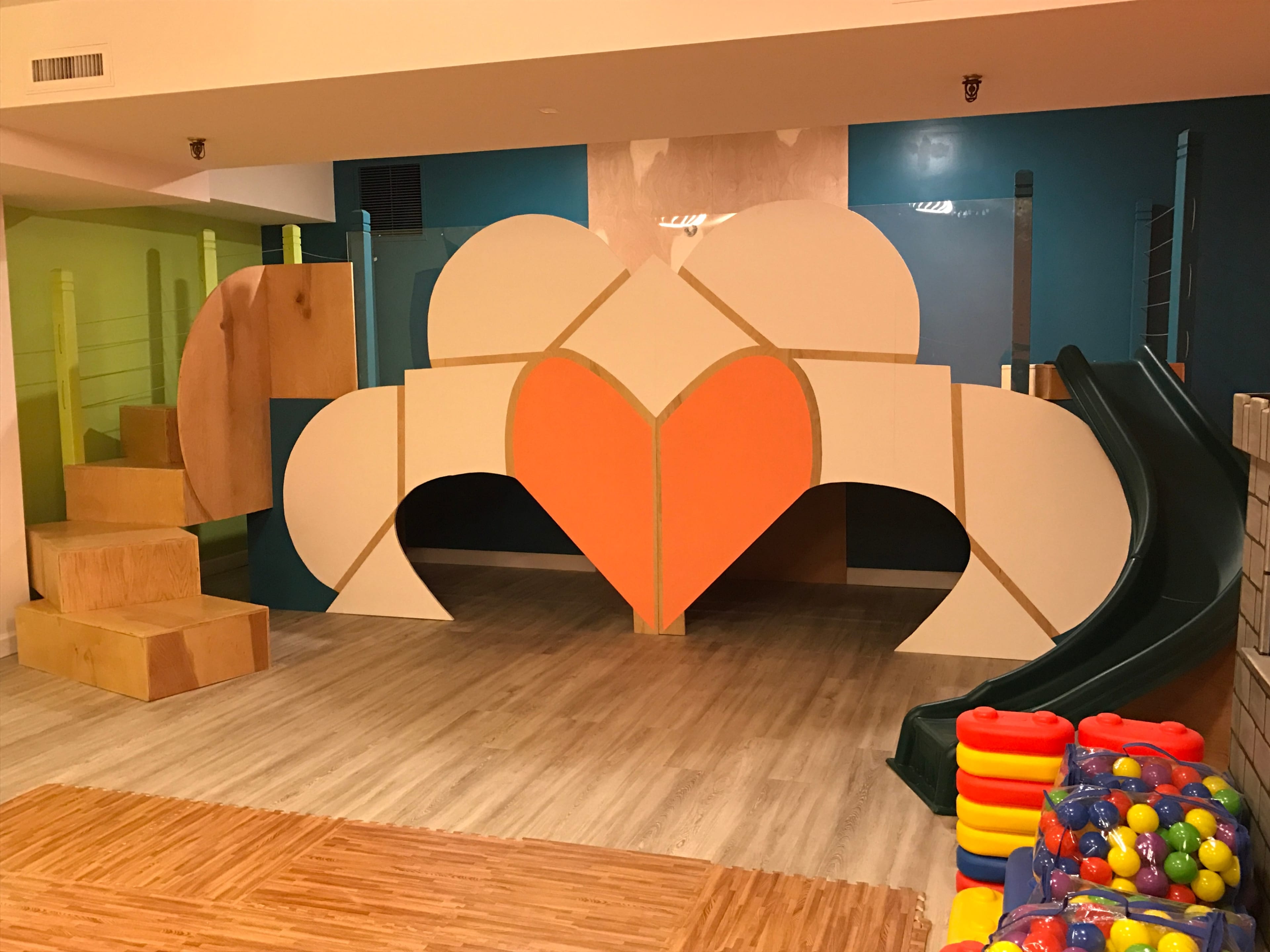 A children's play area featuring a large, colorful climbing structure with a slide, stairs, and various toy blocks.