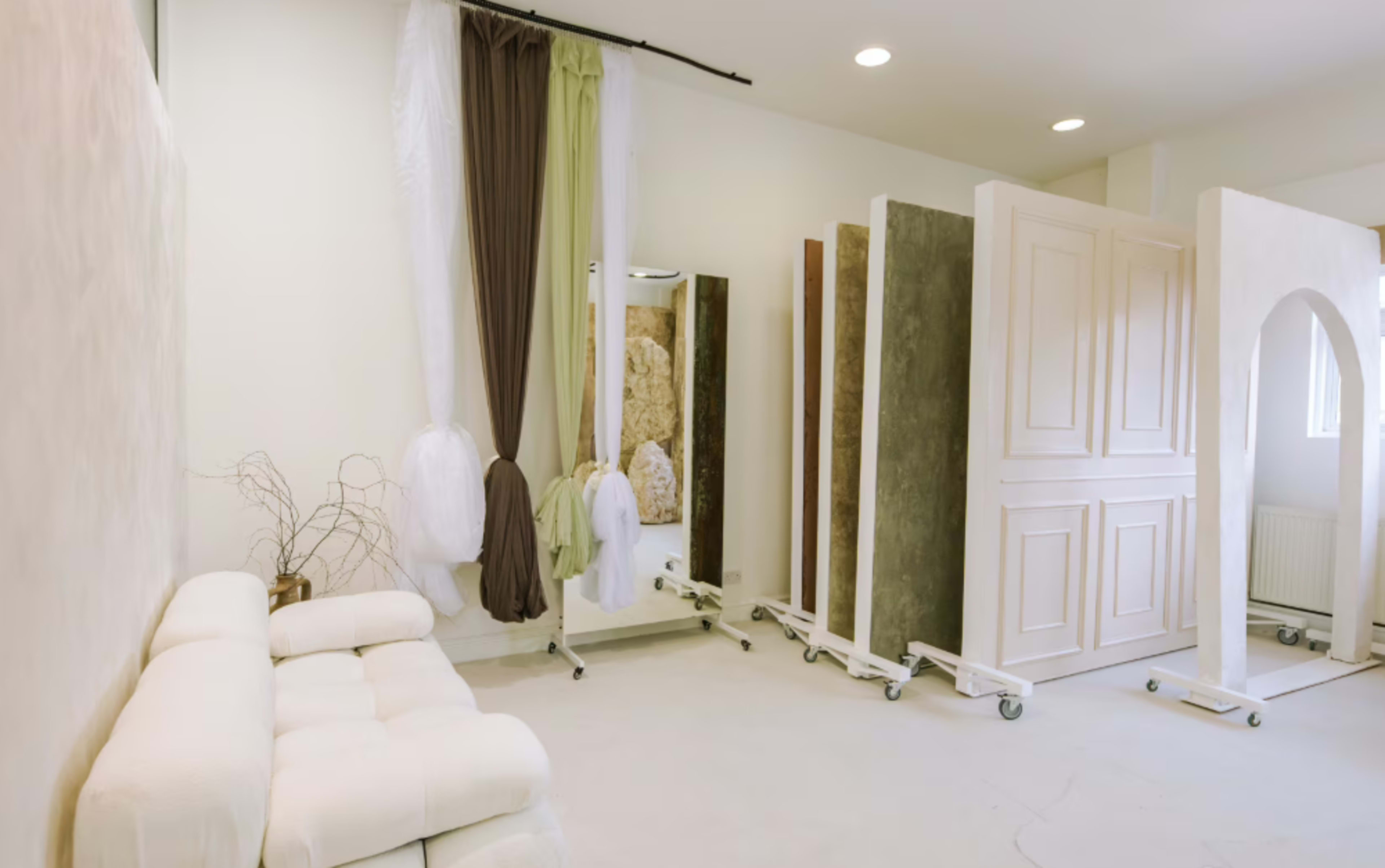 The image shows a bright, minimalist interior space featuring a white sofa, a large mirror, and several movable partition walls.