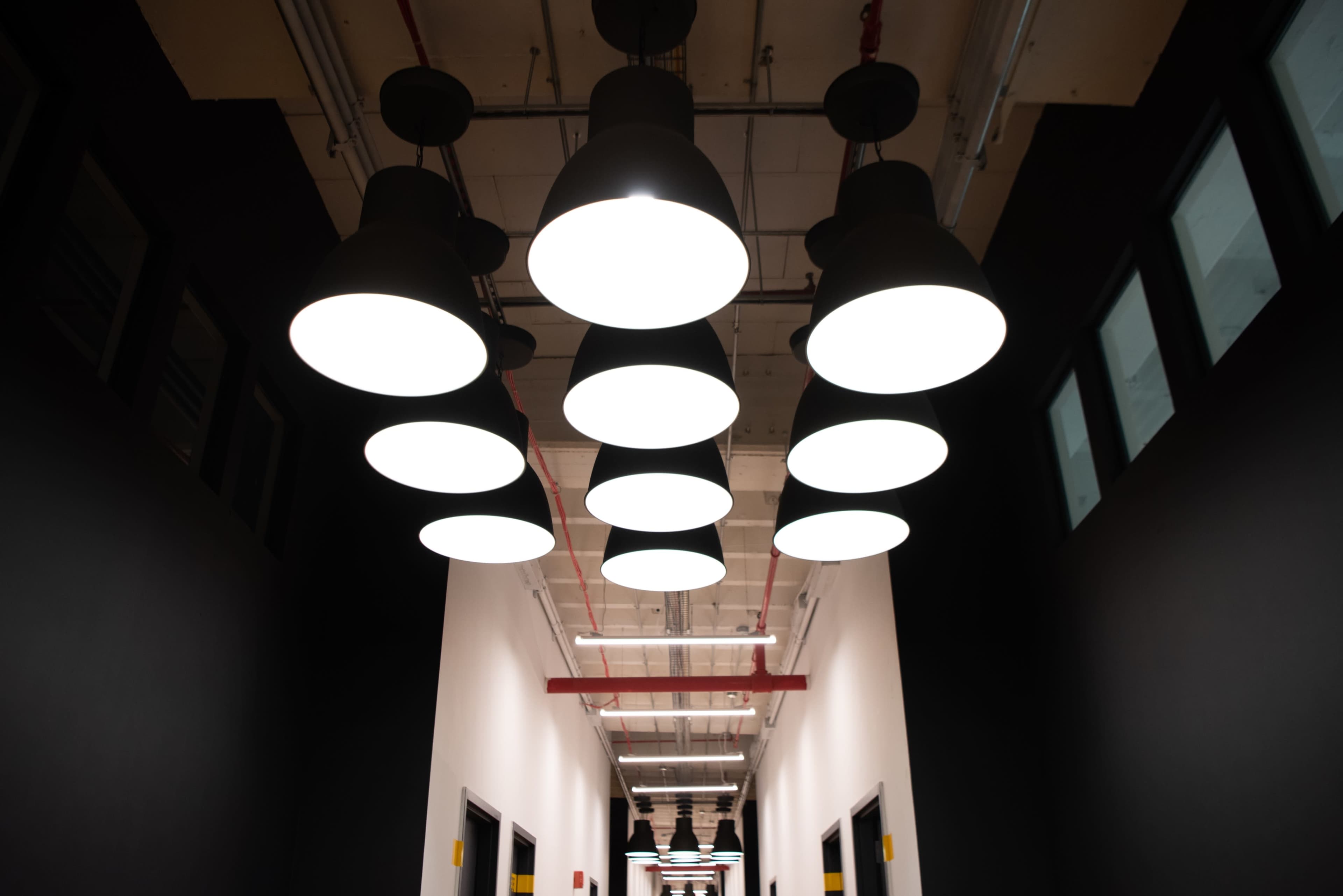 A row of circular pendant lights hangs from the ceiling above a dark hallway with white walls and doors on either side.
