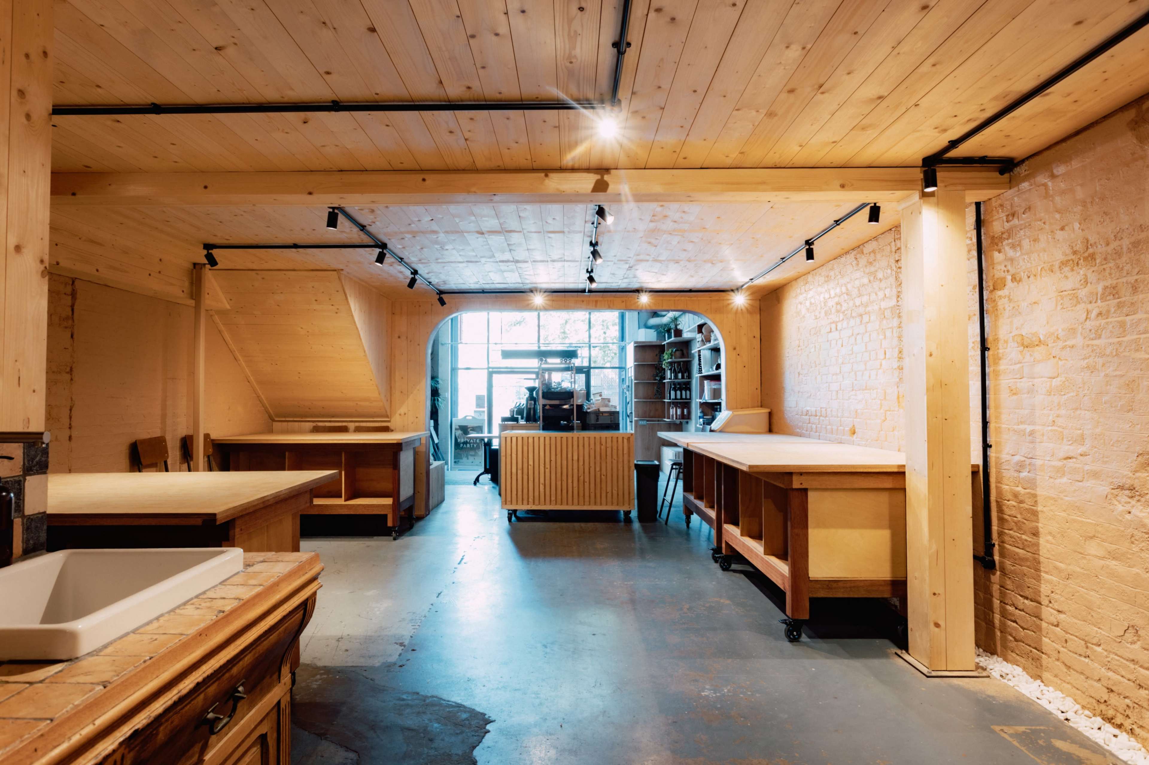 The image shows a spacious interior of a modern workshop or studio, featuring wooden tables, light-colored walls, and large windows that allow natural light to enter.