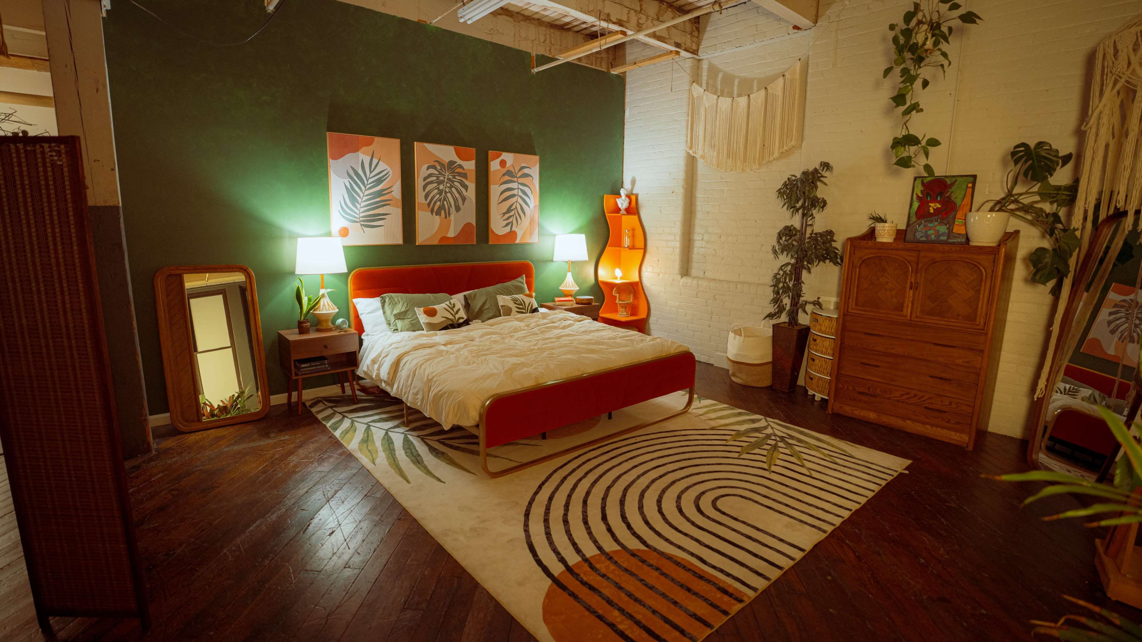 The image shows a decorated bedroom featuring a red bed, a colorful area rug, green accent walls, and various plants and furniture.
