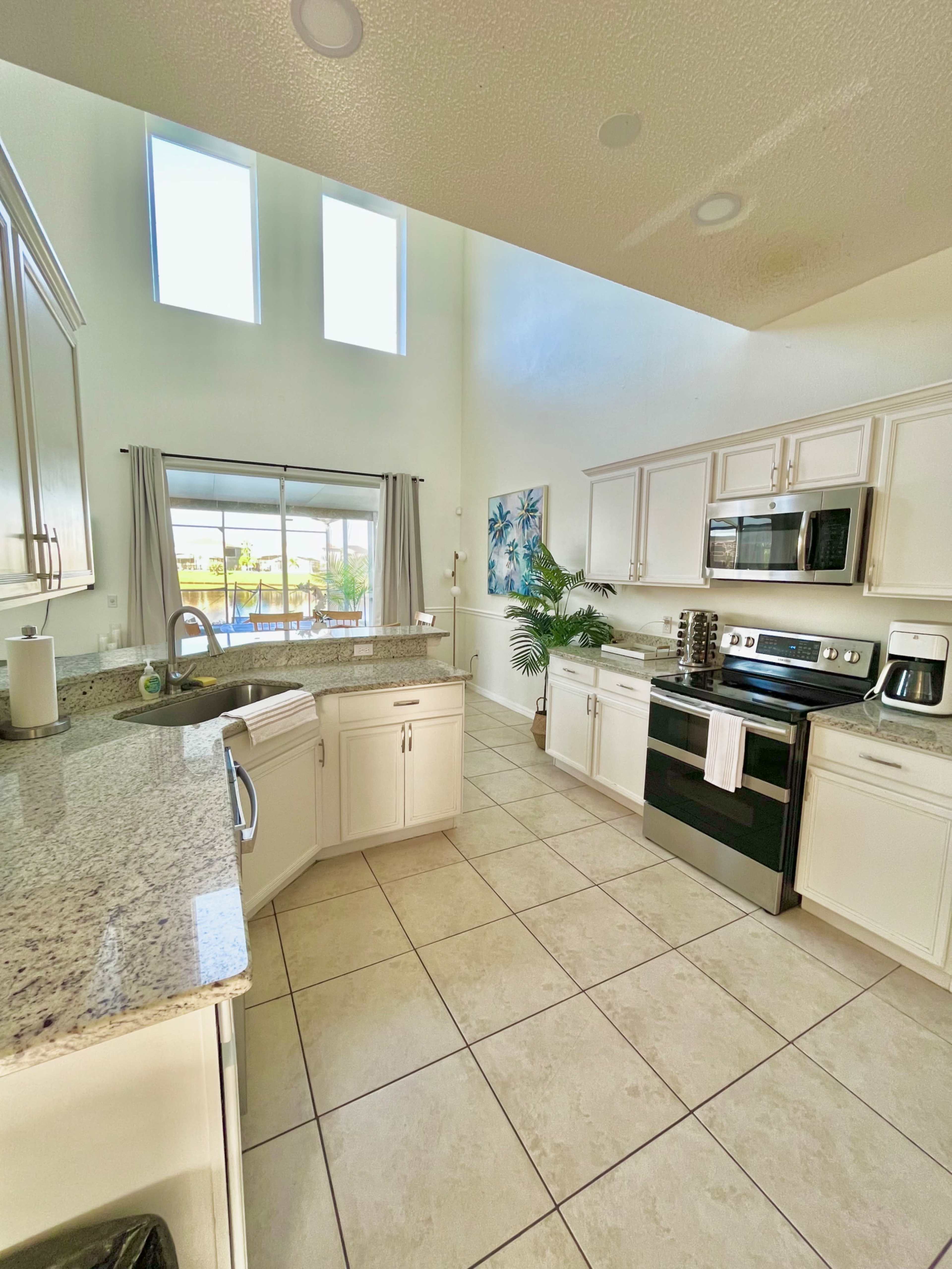 A modern kitchen with white cabinetry, granite countertops, and stainless steel appliances, featuring a large window that lets in natural light.