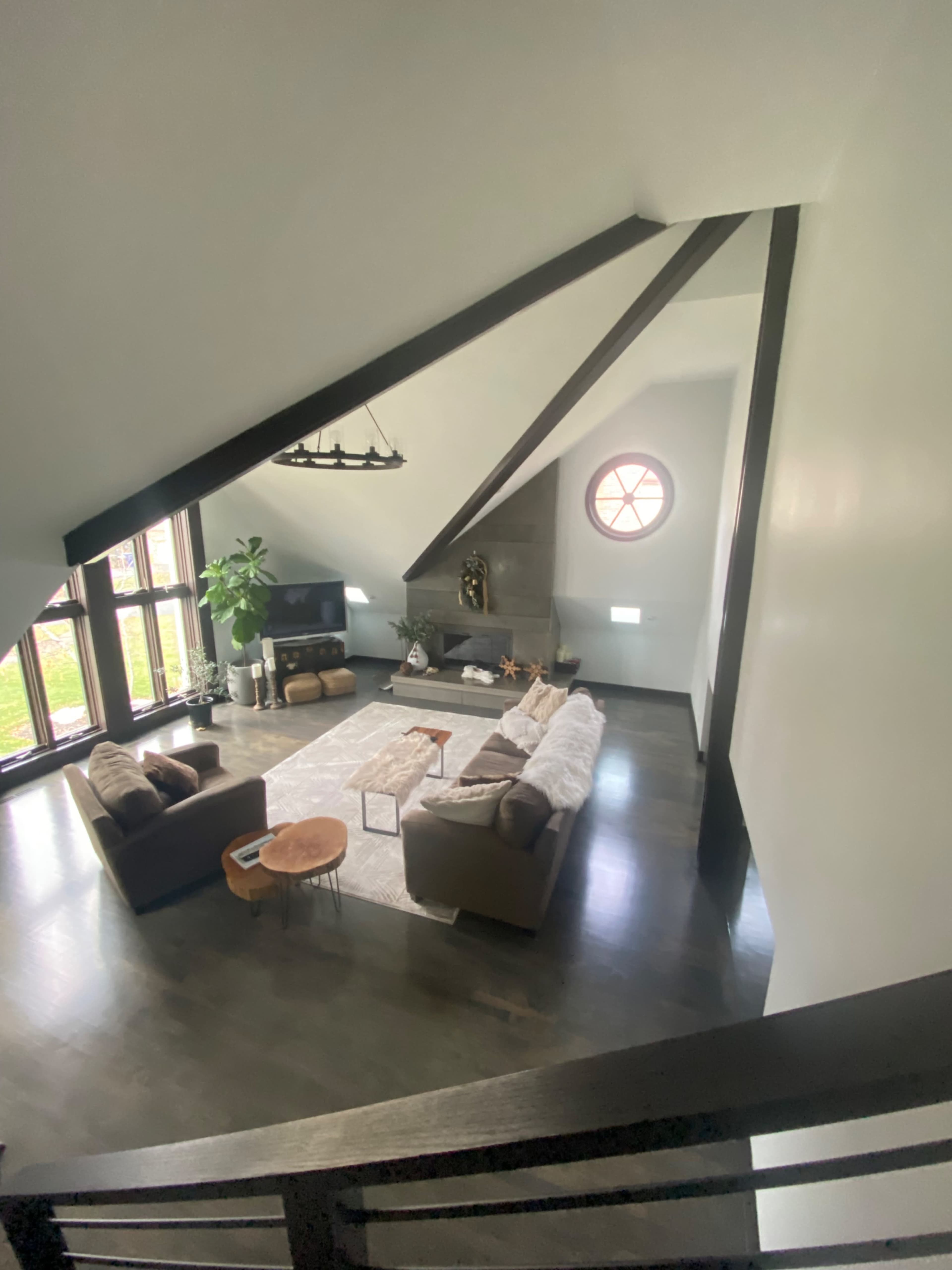 A spacious living room features two sofas, a coffee table, a television, and large windows with a round window above a stone fireplace.