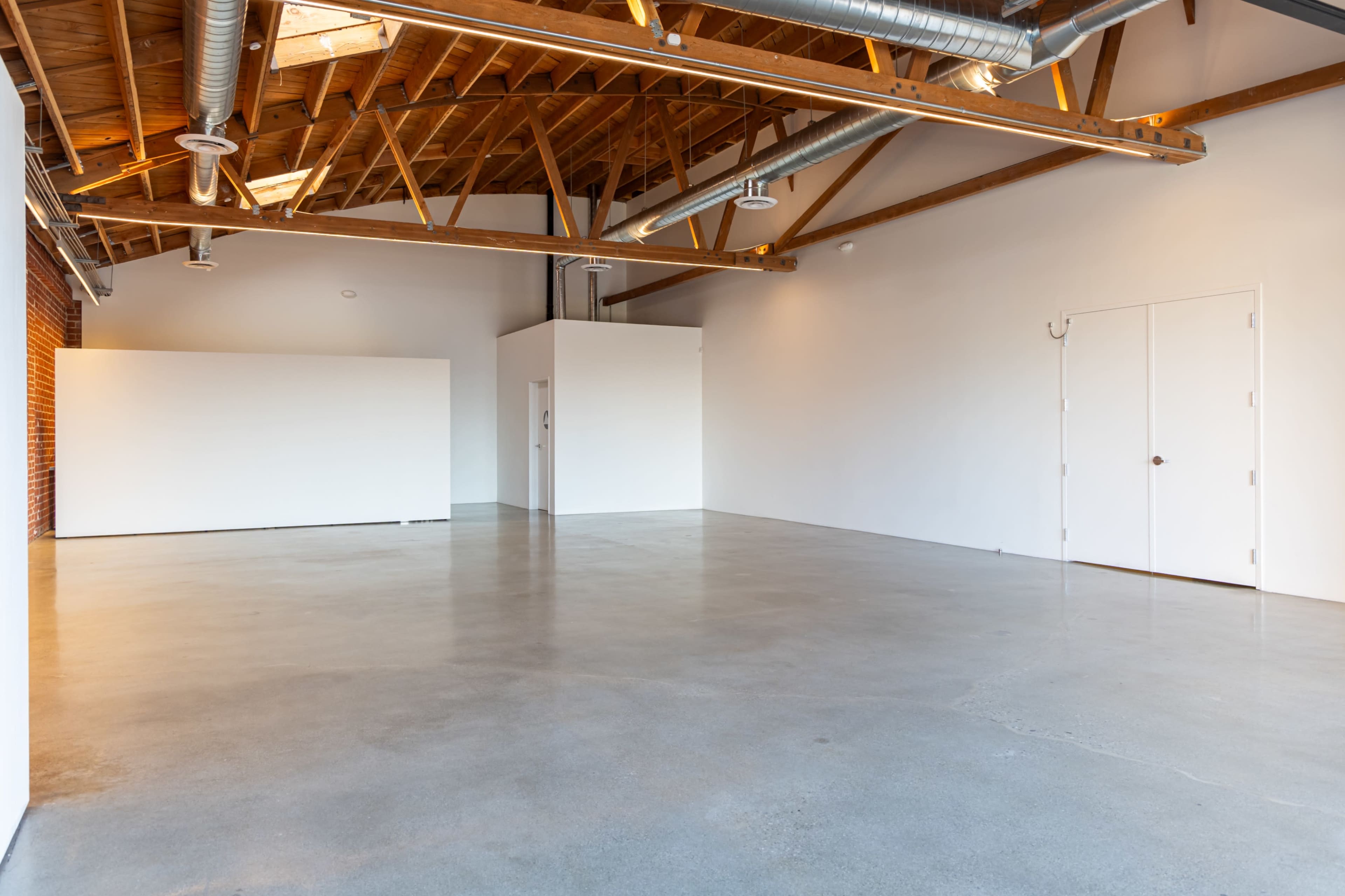 The image shows an empty industrial-style interior space with a polished concrete floor and exposed wooden beams on the ceiling.
